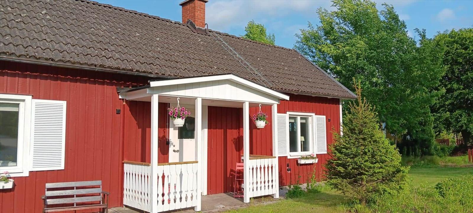 Rotes Haus mit weißem Vordach, Blumenkästen und Holzbank im Garten.