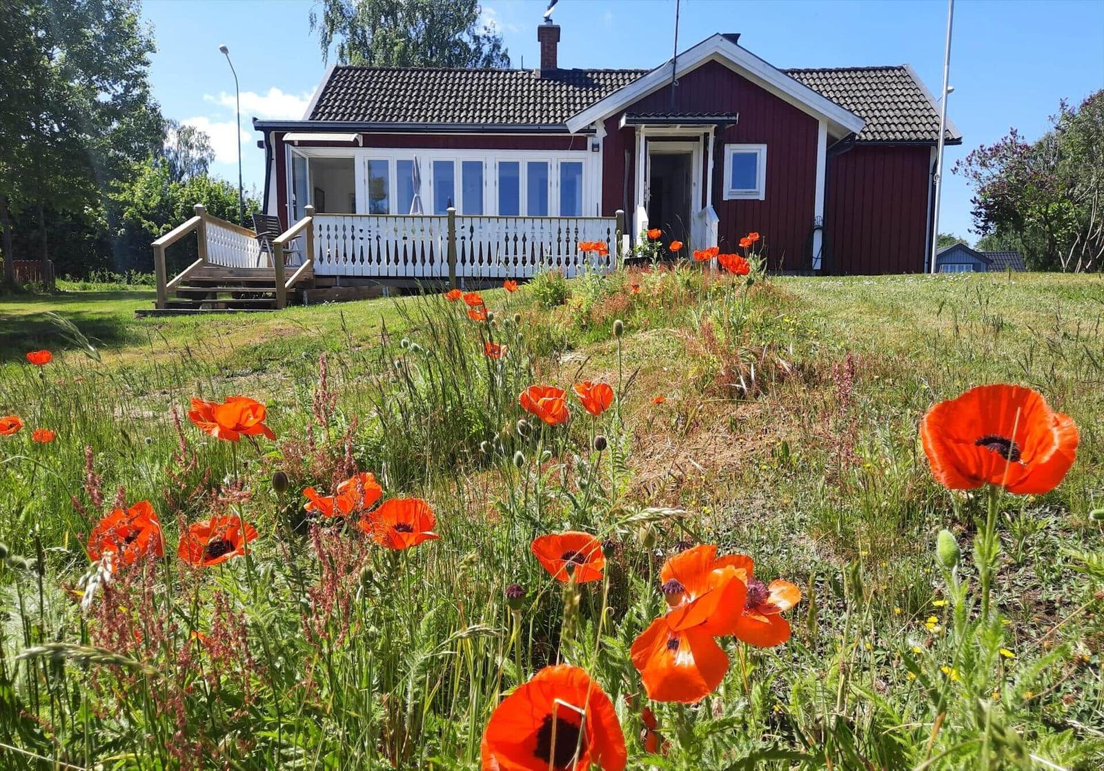 Rotes Haus mit weißem Balkon und Blumenfeld im Vordergrund.