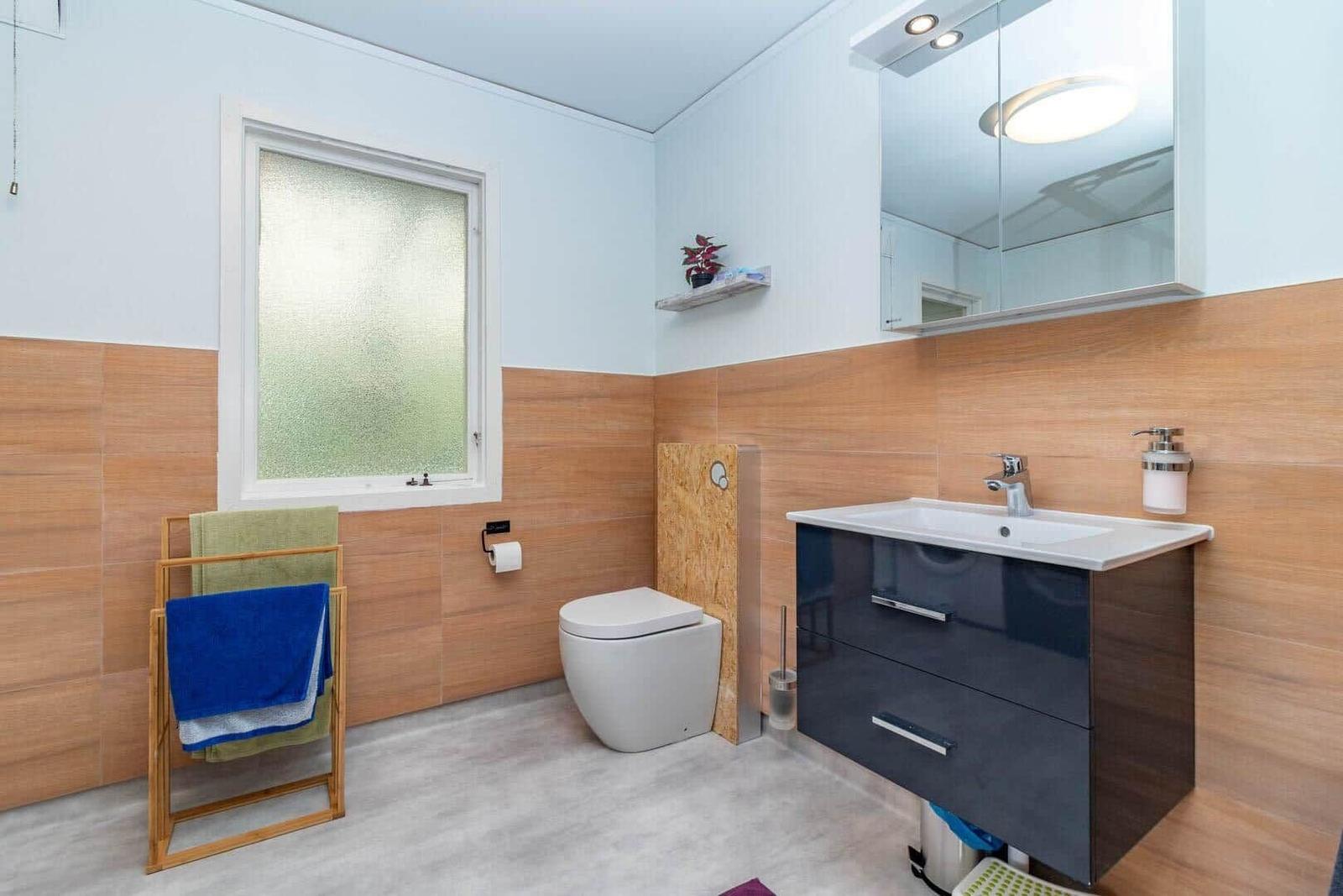 Badezimmer mit Toilette, Waschbecken und Fenster. Holzwand und Spiegelschrank.