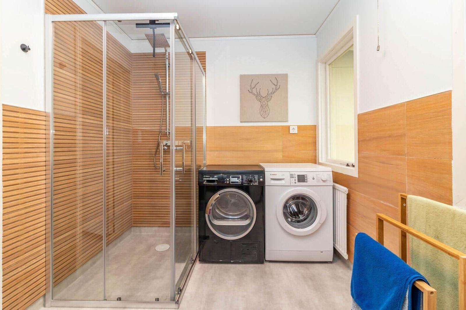 Dusche mit Glaswand, Waschmaschine und Trockner in modernem Badezimmer.