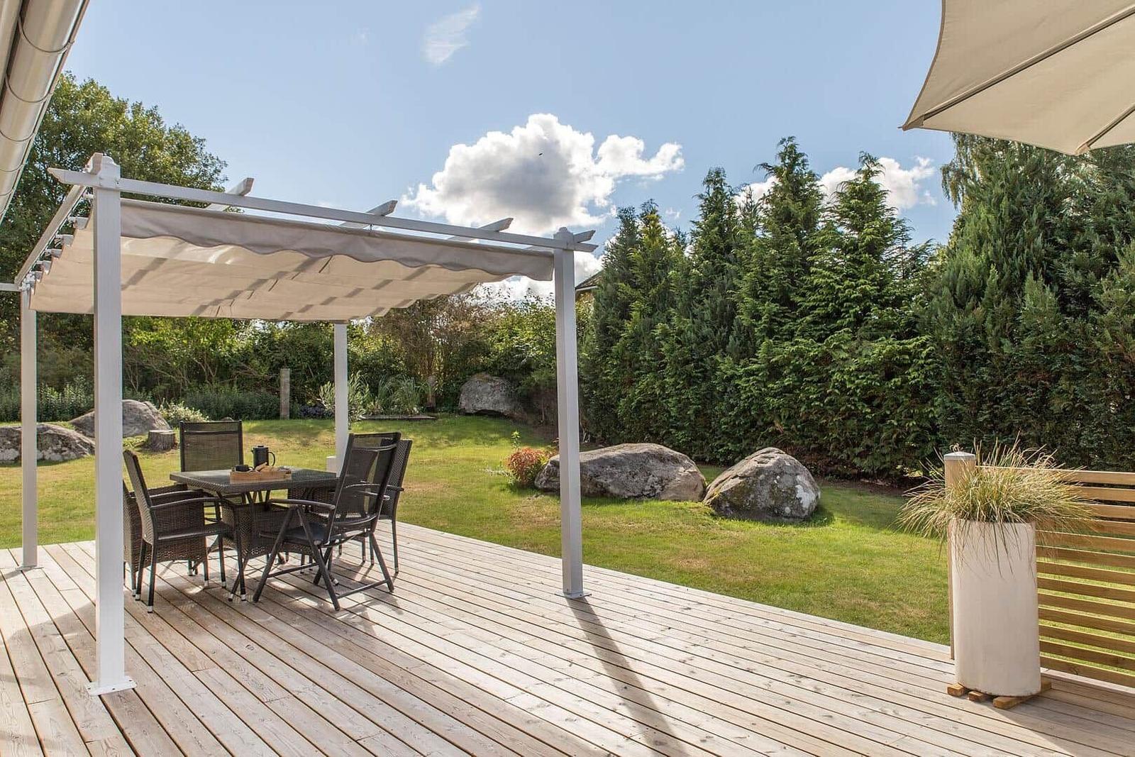 Terrasse mit Pavillon, Tisch und Stühlen. Grünfläche mit Bäumen und Felsen im Hintergrund.