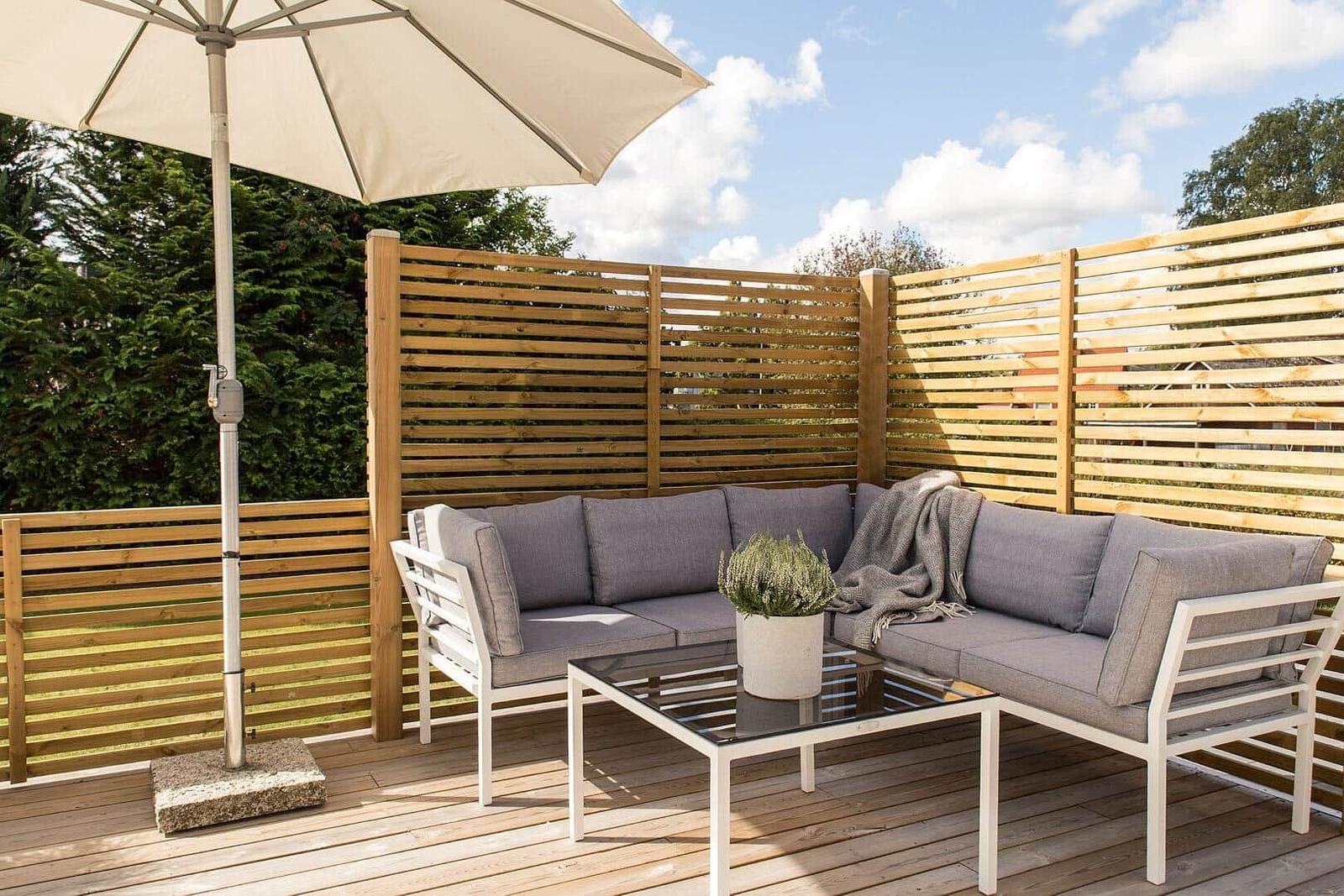 Terrasse mit Sitzgruppe, Sonnenschirm und Holzgeländer.
