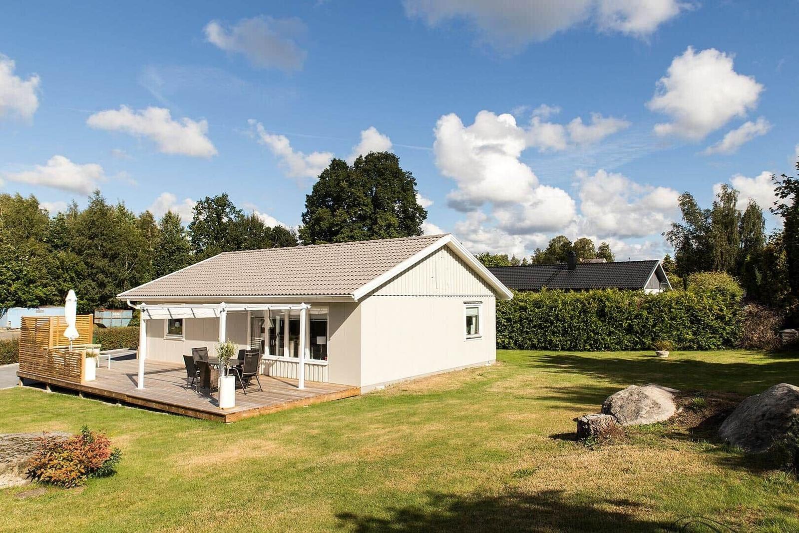 Ein Ferienhaus mit Terrasse, Garten und Blick auf Bäume unter blauem Himmel.
