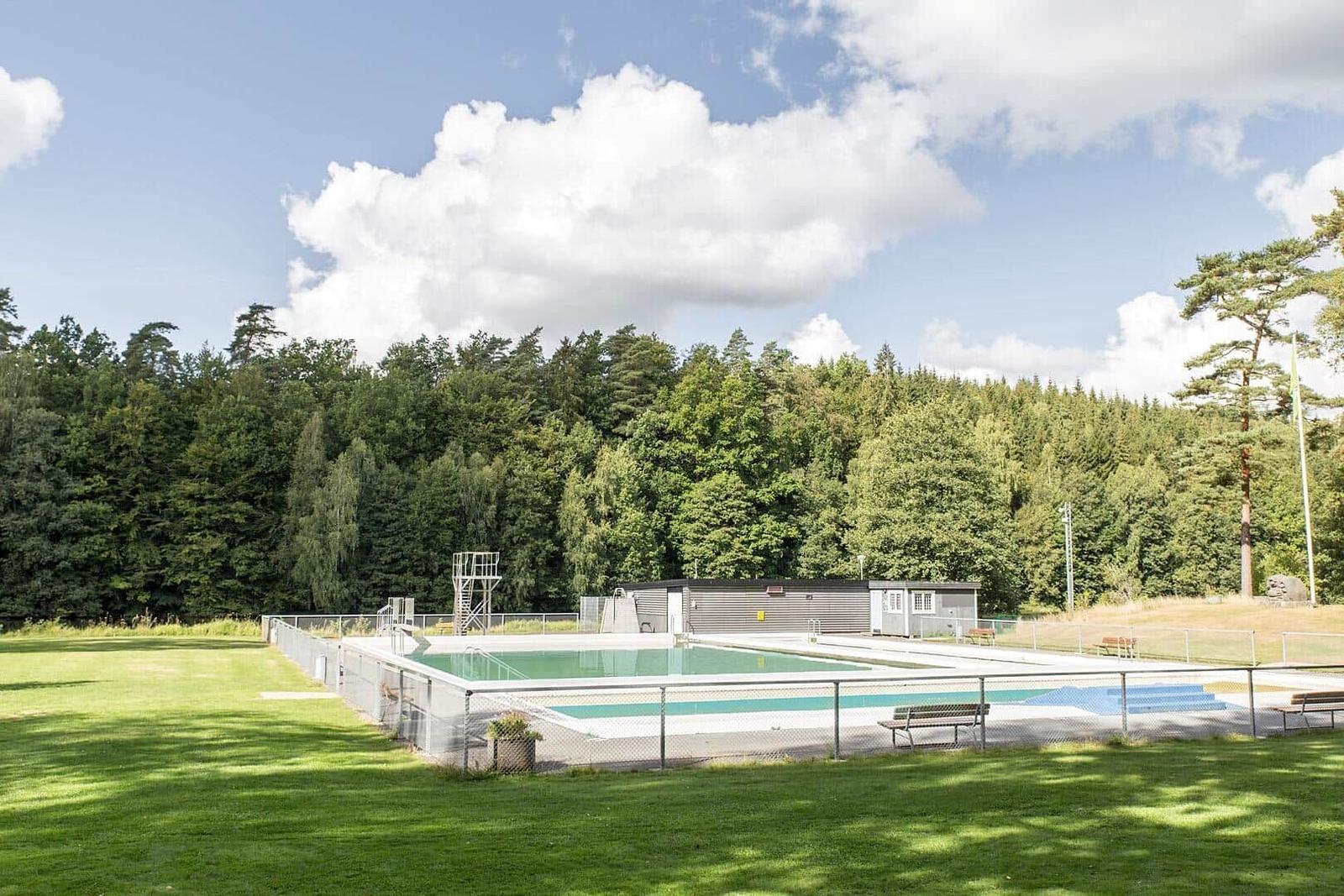 Ein Schwimmbad mit Sprungturm und Umzäunung im Grünen.