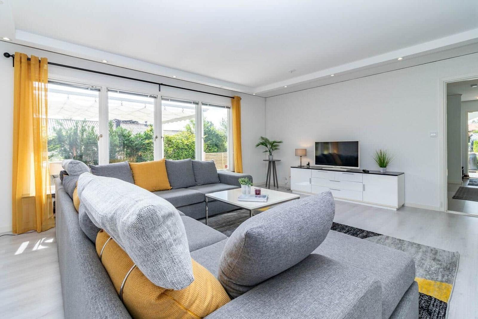 Wohnzimmer mit grauem Sofa, gelben Kissen und großem Fenster zur Terrasse.