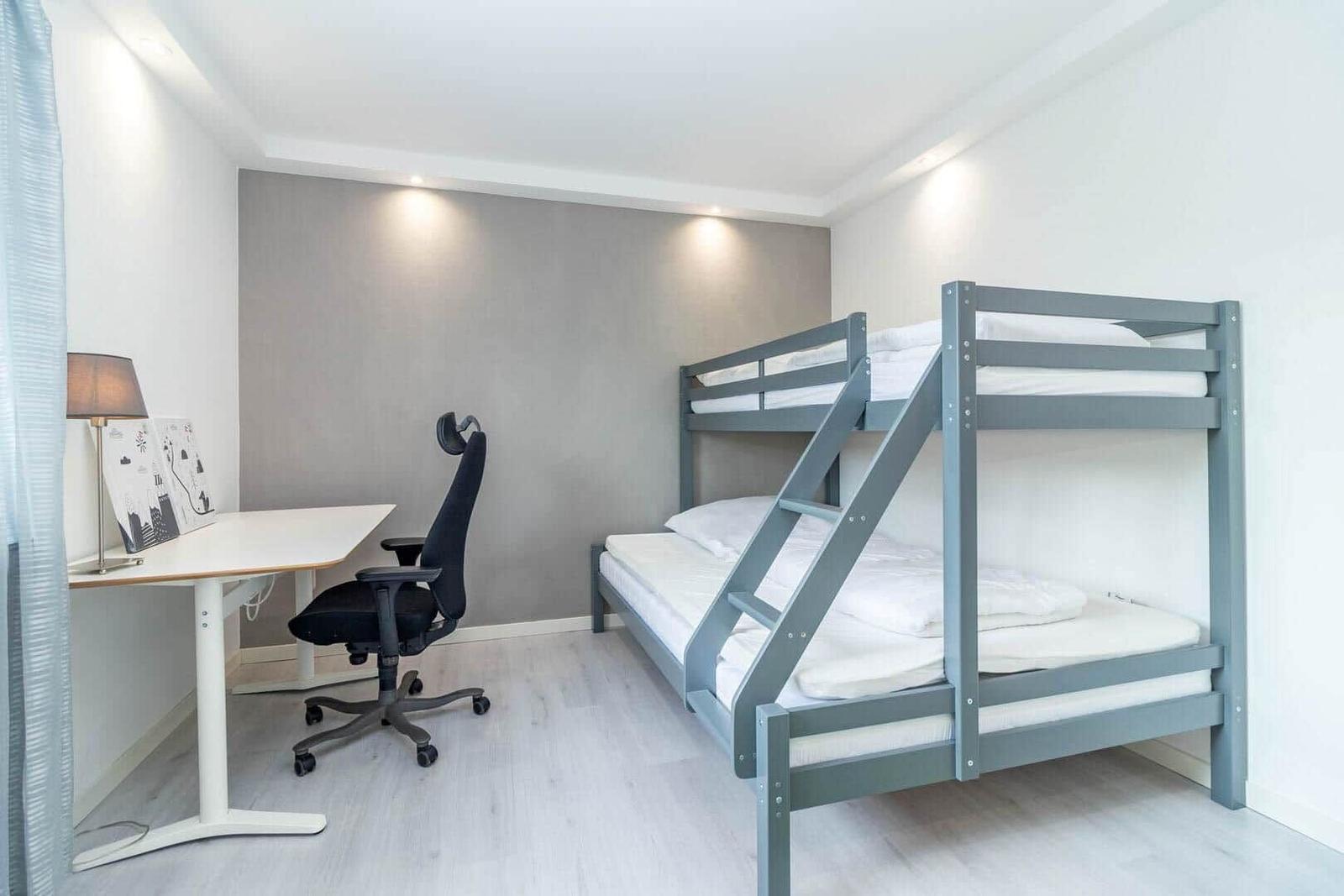 Zimmer mit Doppelstockbett und Schreibtisch mit Stuhl.