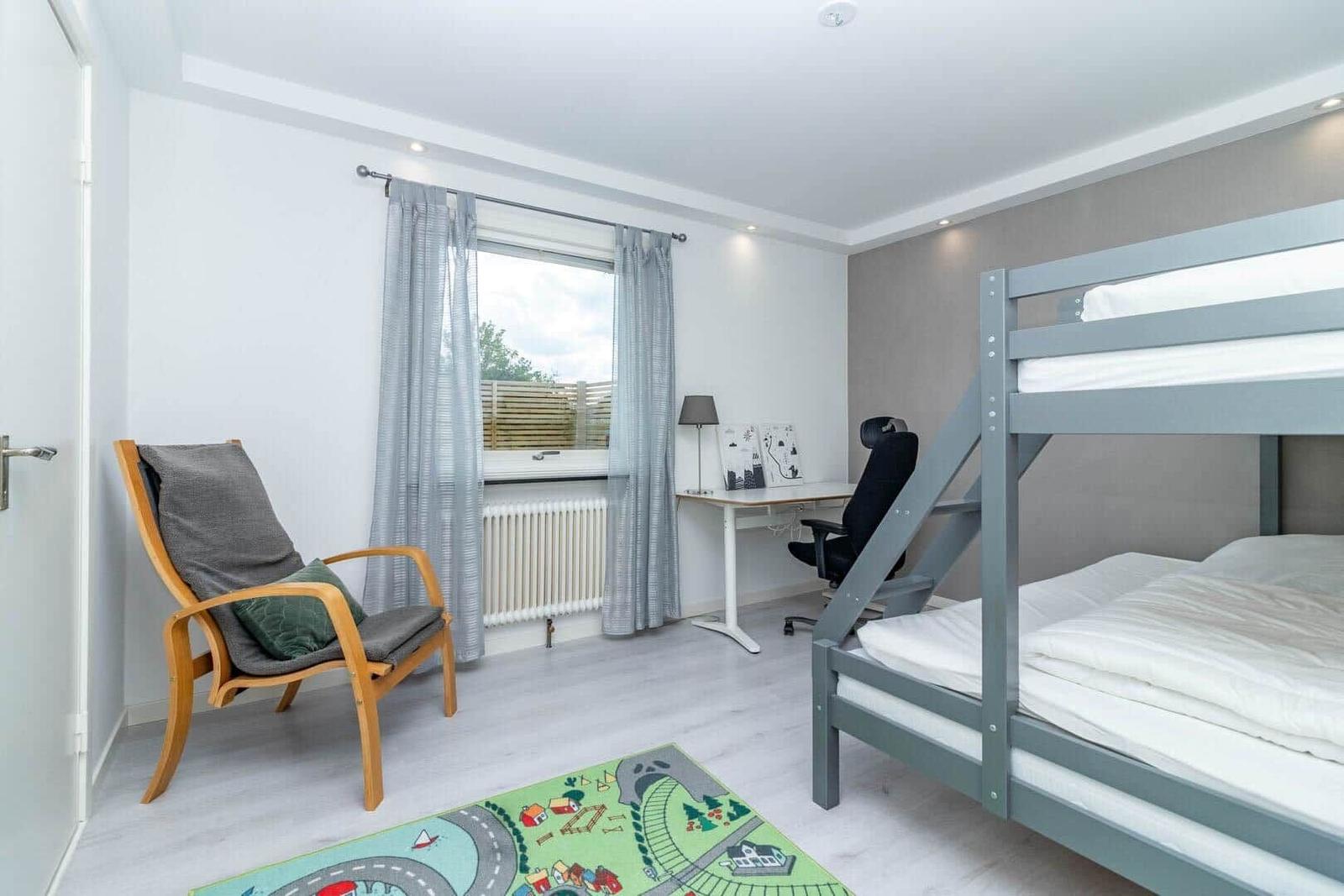 Zimmer mit Doppelstockbett, Schreibtisch und Sitzgelegenheit. Fenster mit Gardinen.