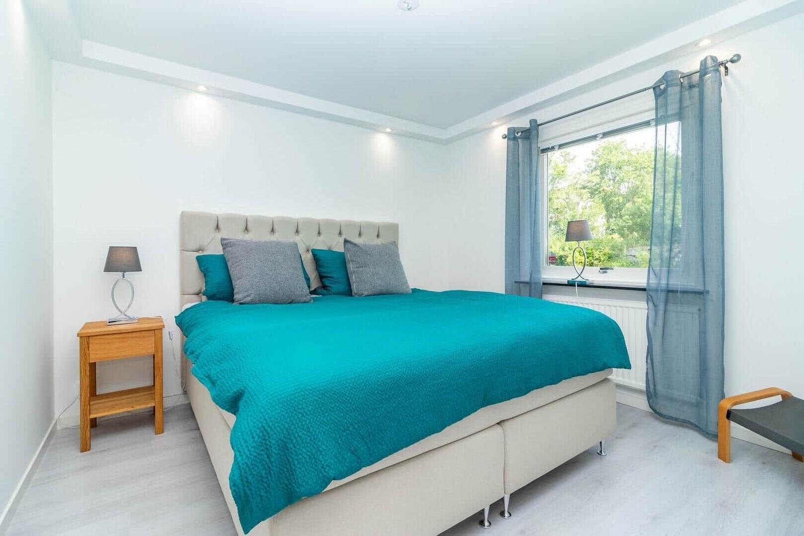 Schlafzimmer mit Bett, Nachttisch und Fenster mit Blick auf Grün.