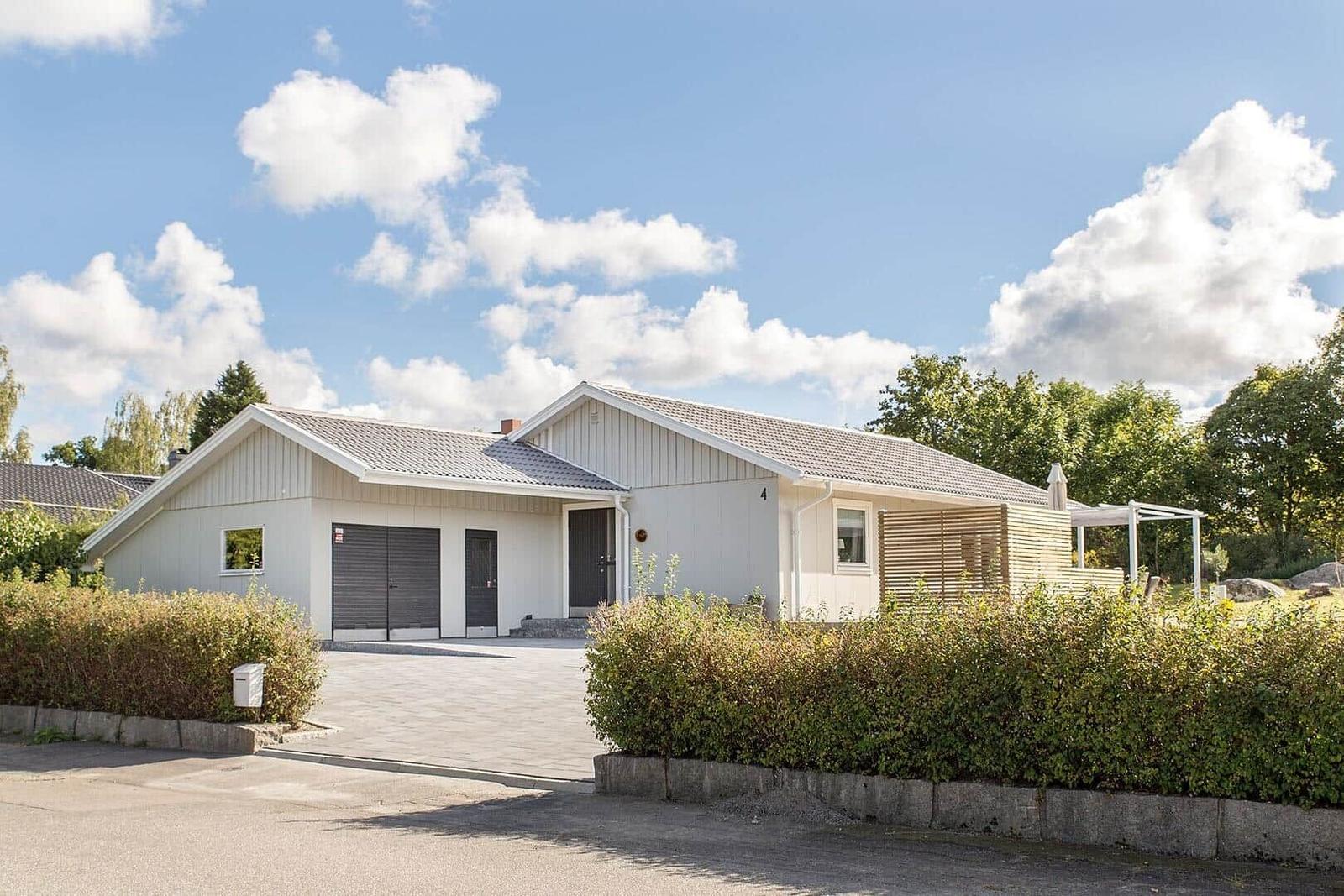Moderne Villa mit Garage, Terrasse und grüner Umgebung unter blauem Himmel.