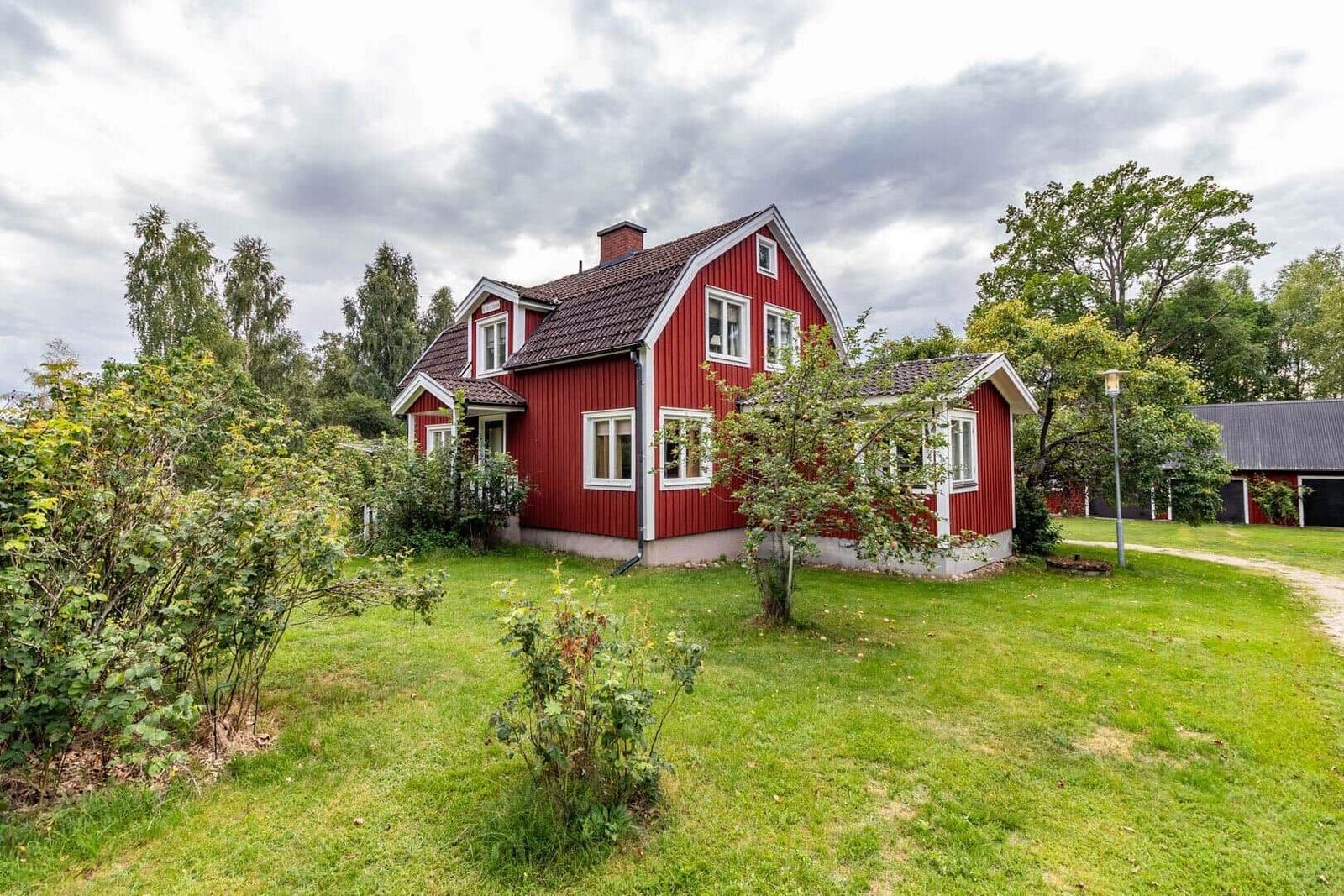 Rotes Holzhaus mit grünem Garten und Bäumen im Hintergrund.