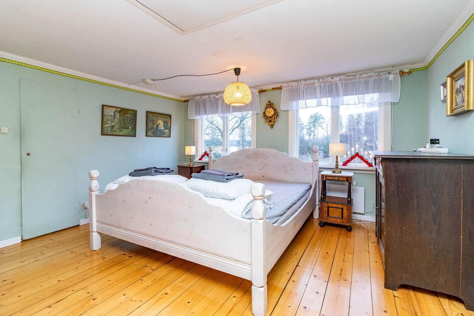 Schlafzimmer mit Bett, Nachttischen und Fenster. Holzboden und hellblaue Wände.