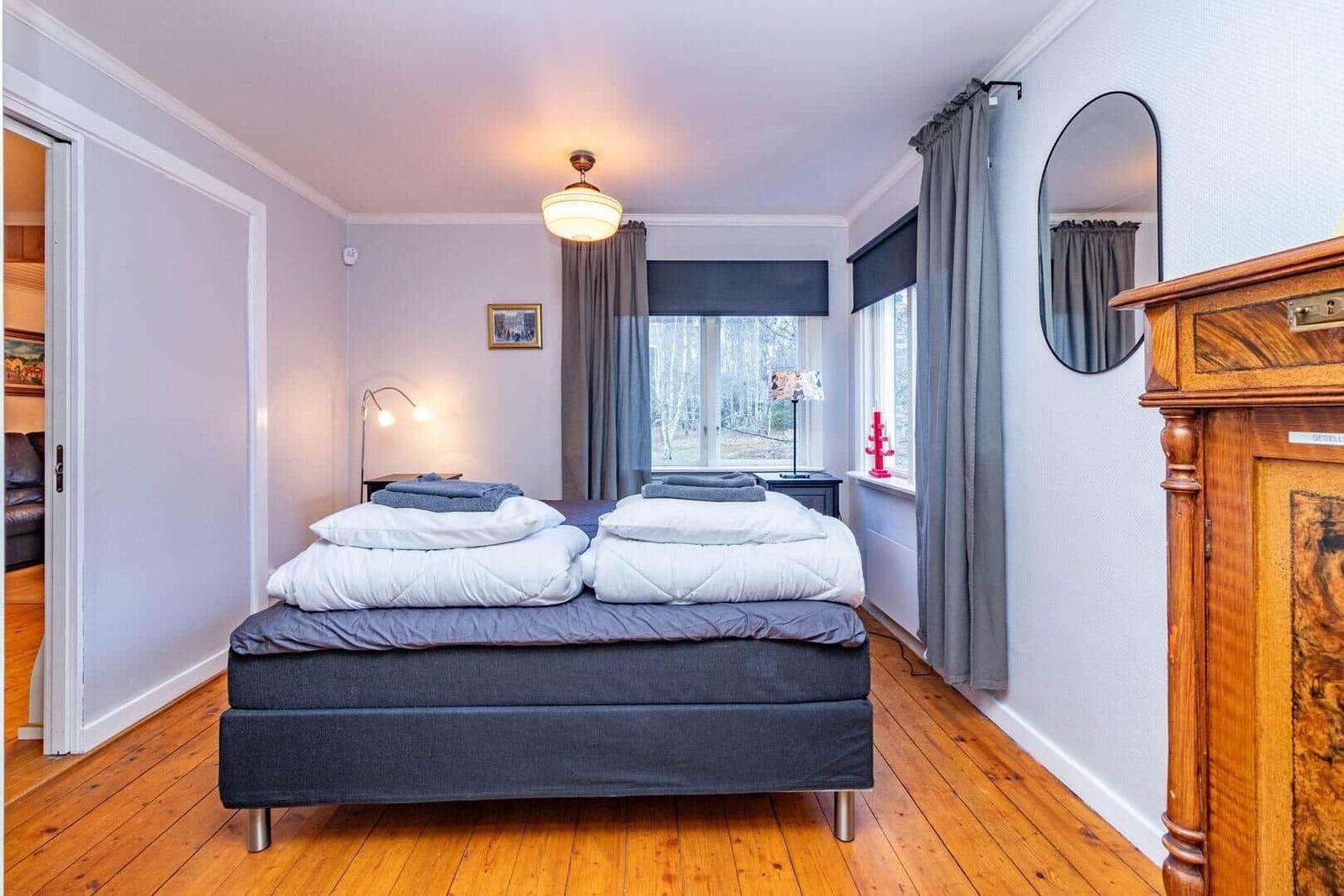 Schlafzimmer mit Bett, Fenster und Holzboden. An der Wand hängt ein Spiegel.