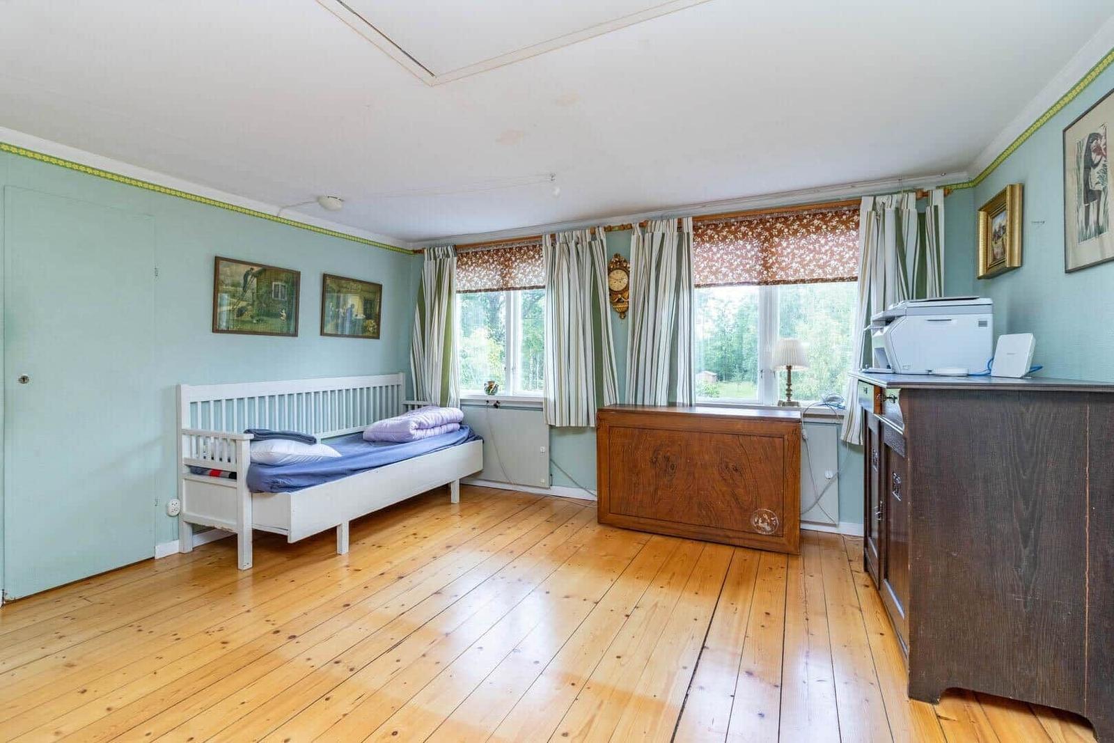Ein Schlafzimmer mit Holzboden, weißem Bett und Holzschränken. Fenster mit Vorhängen.