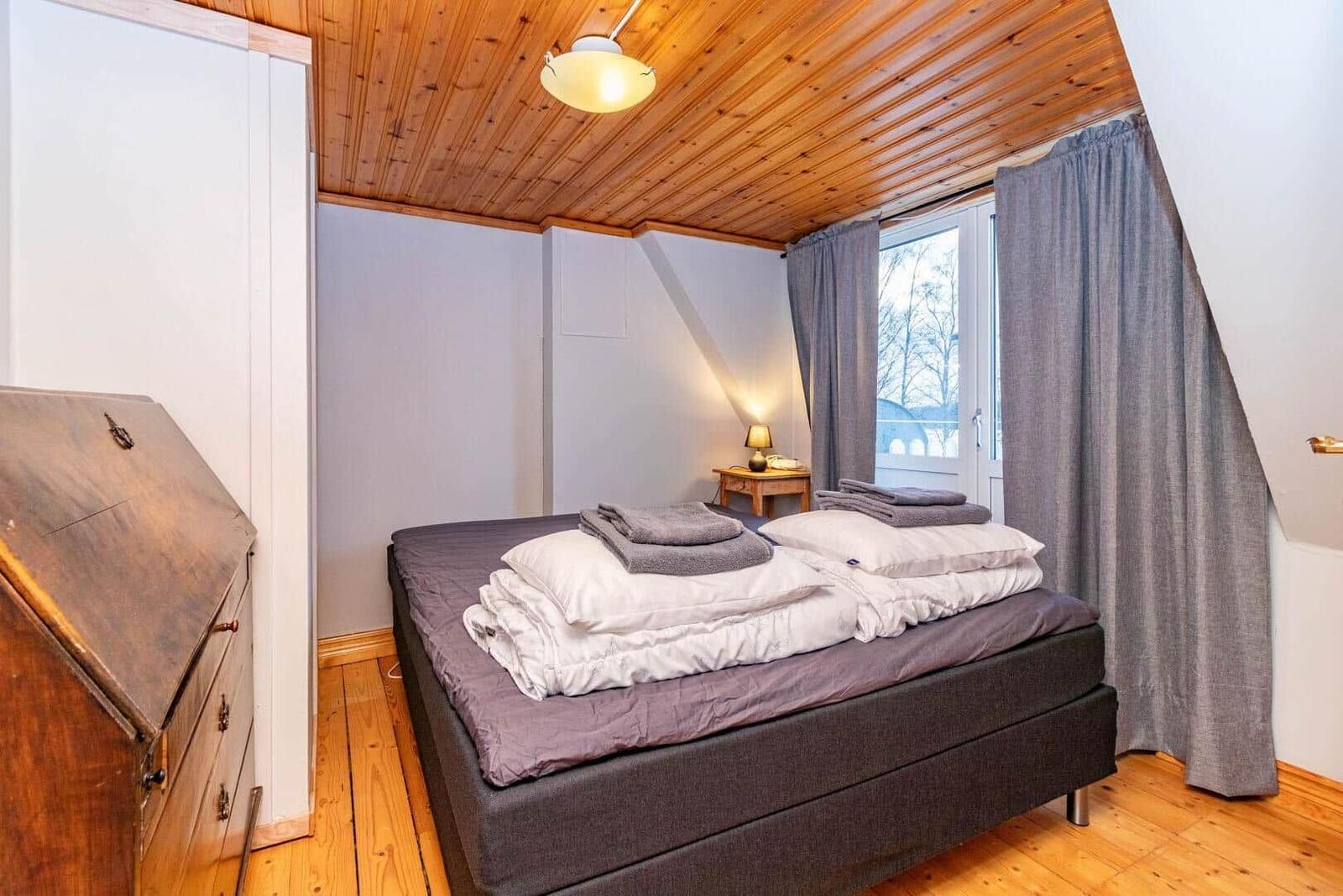 Schlafzimmer mit Bett, Holzdecke und Fenster mit Vorhängen.