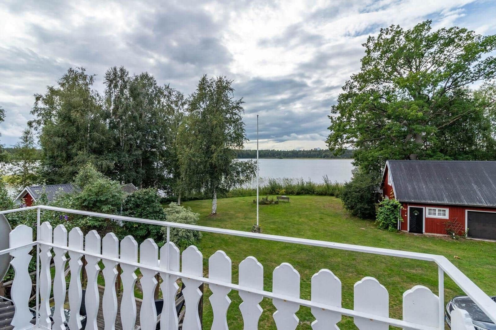 Weitläufiger Garten mit Blick auf See und rote Scheune. Weiße Brüstung im Vordergrund.