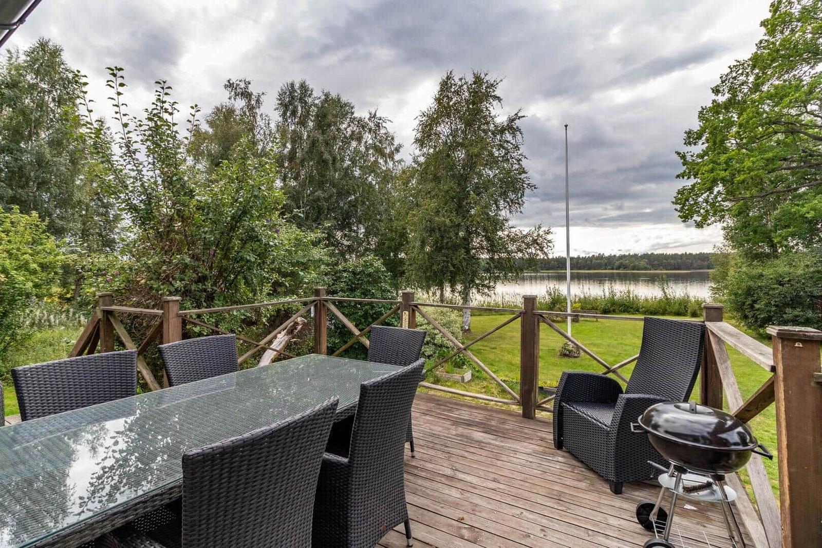 Terrasse mit Tisch, Stühlen und Grill, Blick auf See und Bäume.