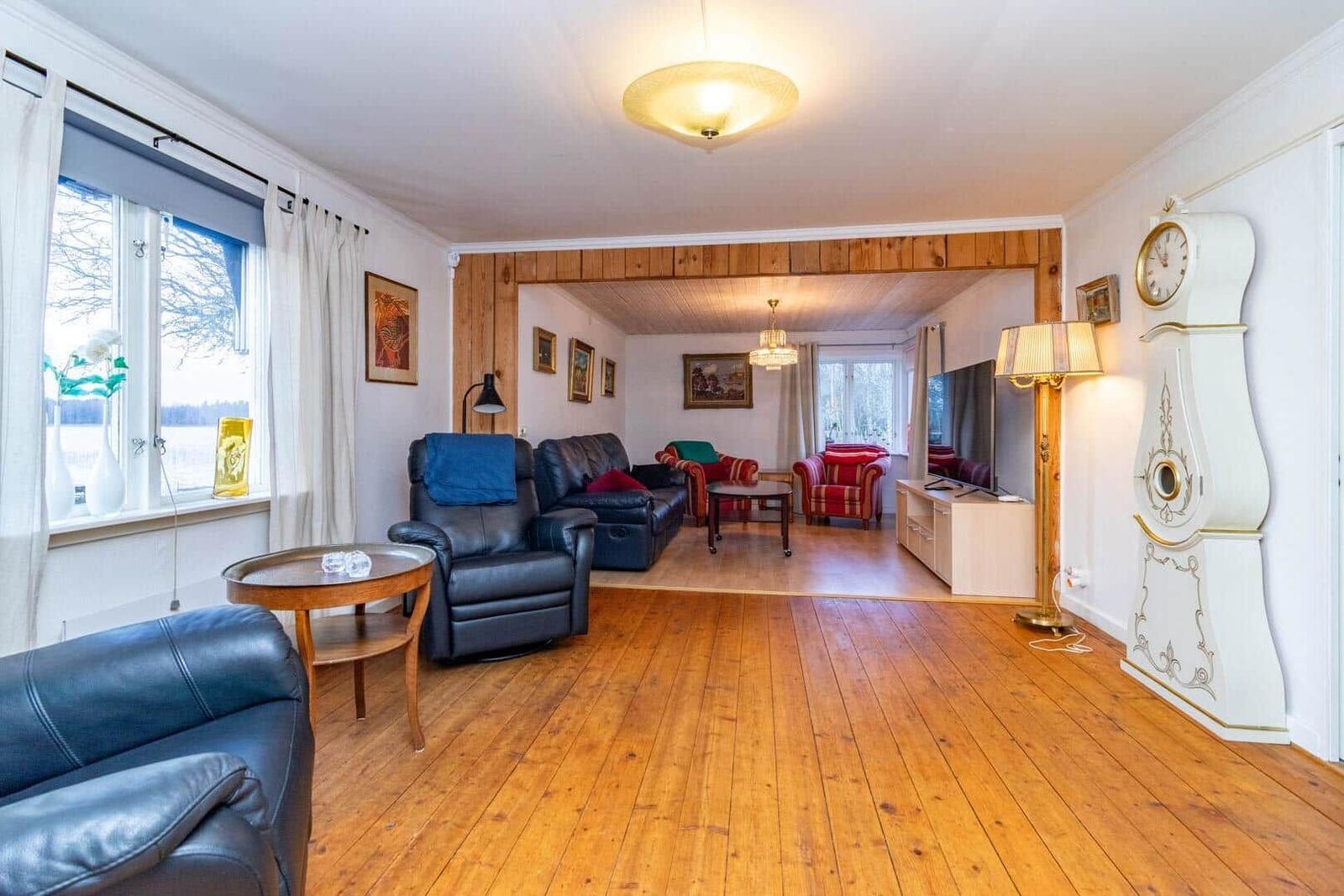 Wohnzimmer mit Holzboden, Ledersofa und Stehlampe. Durchgang zum Essbereich mit TV und Uhr.
