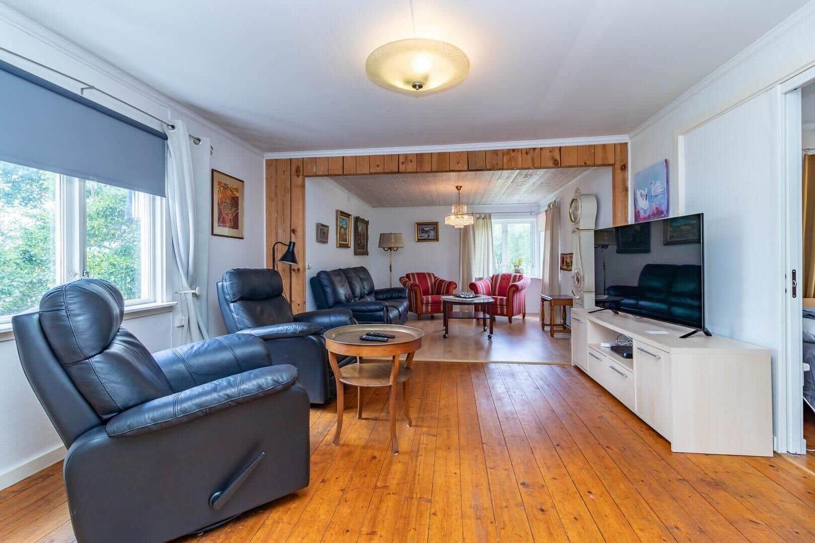 Wohnzimmer mit Ledersofa, Holzboden und Fernseher. Blick in angrenzenden Raum mit Stühlen.