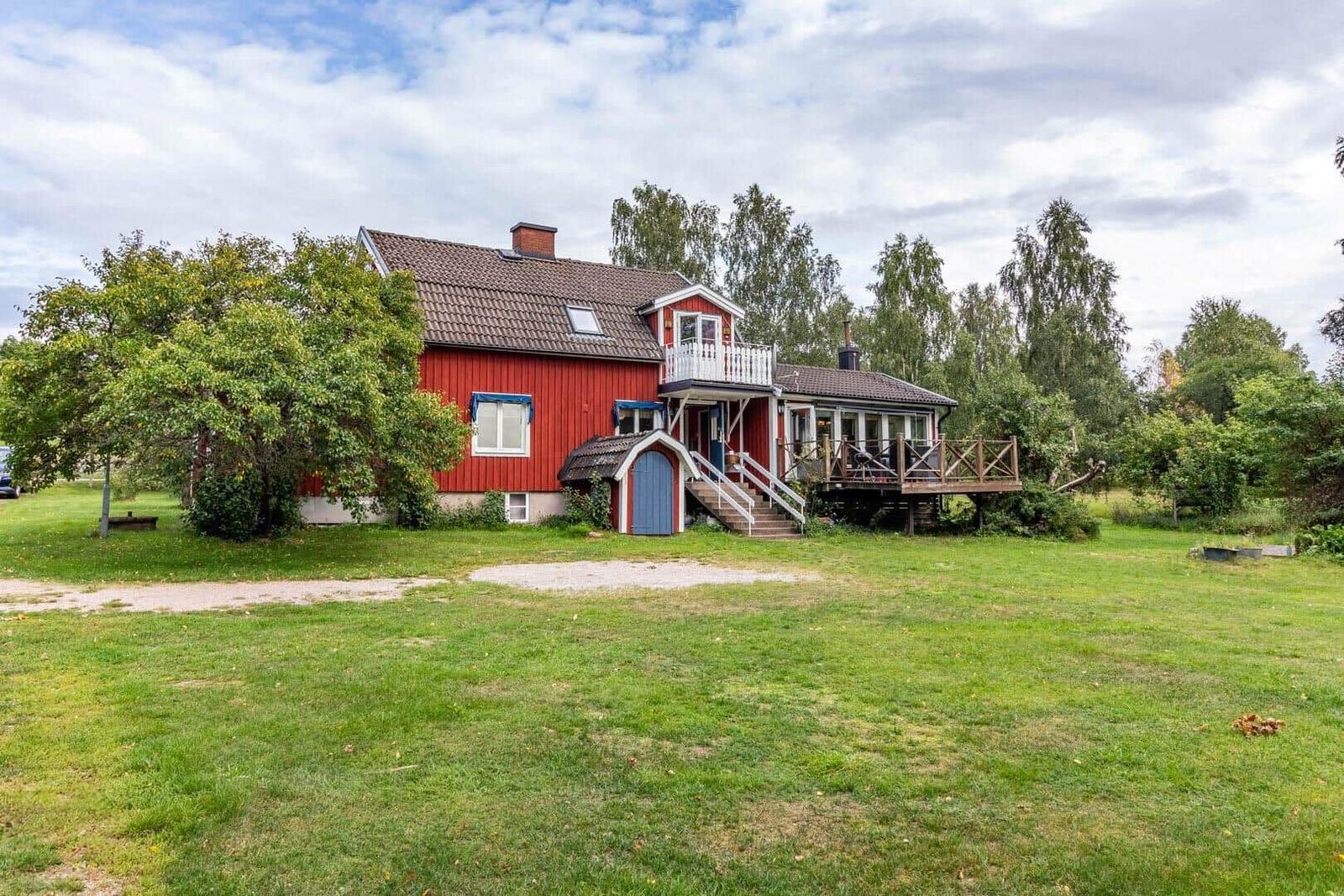 Rotes Haus mit Terrasse und Garten. Umgeben von Bäumen und Gras.