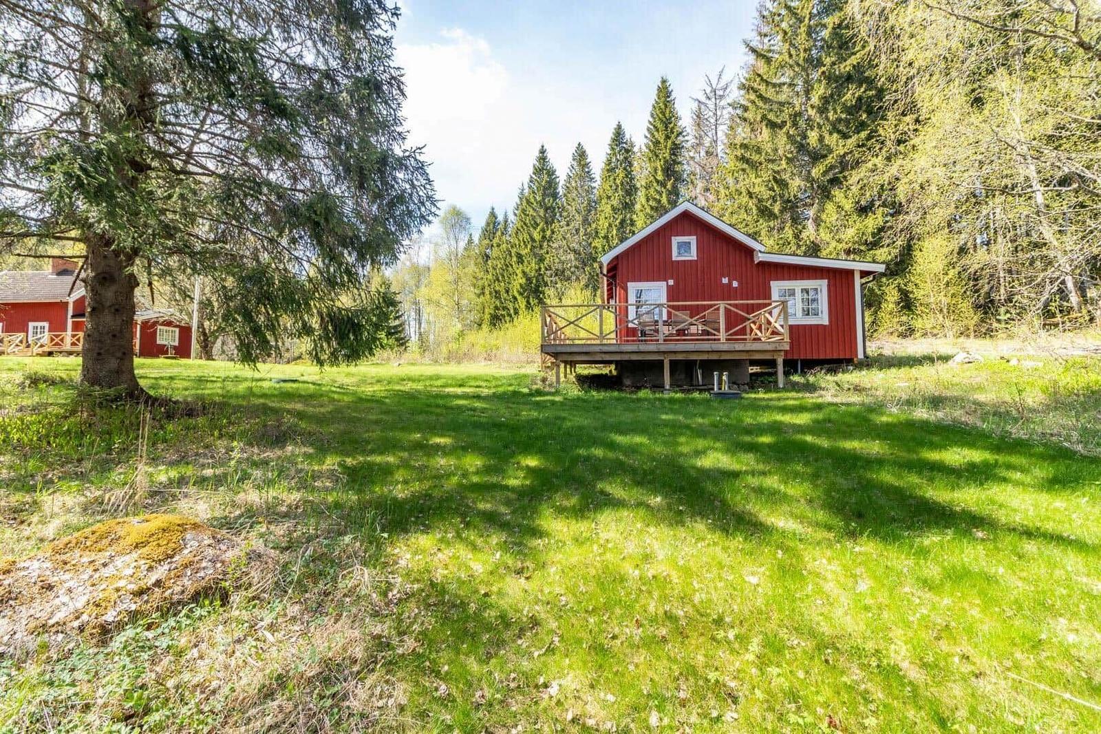 Rotes Holzhaus mit Balkon steht auf grünem Grundstück zwischen Bäumen.