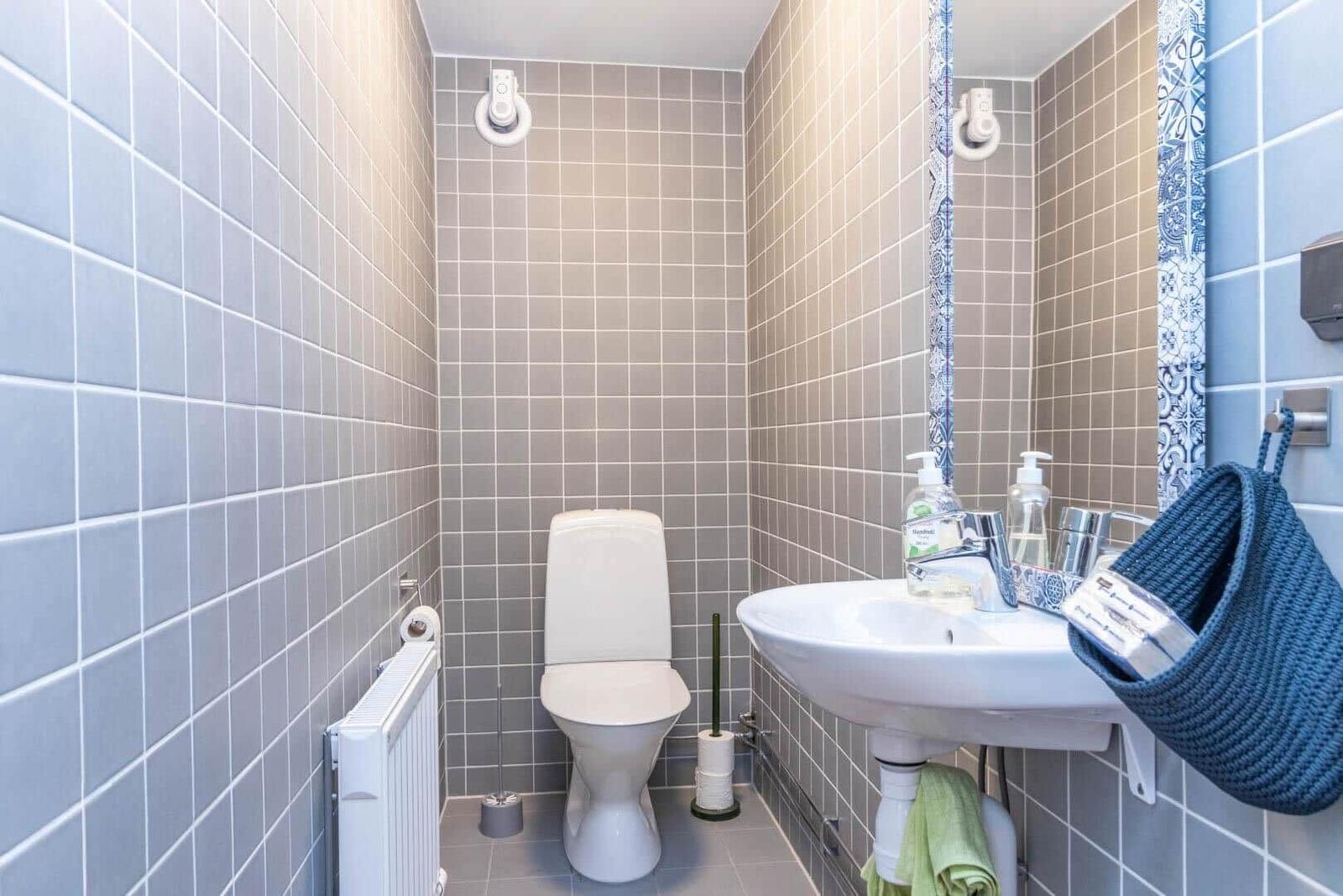 Badezimmer mit Toilette, Waschbecken und Spiegel. Wände sind mit Fliesen verkleidet.
