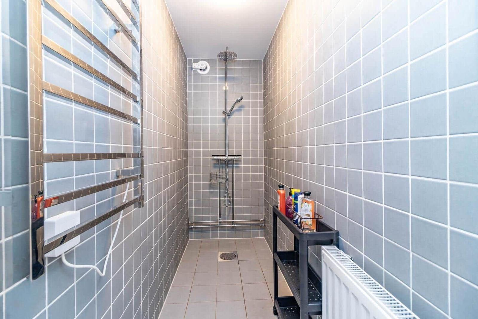 Dusche mit Duschbrause, Handtuchhalter und Regal mit Badartikeln.