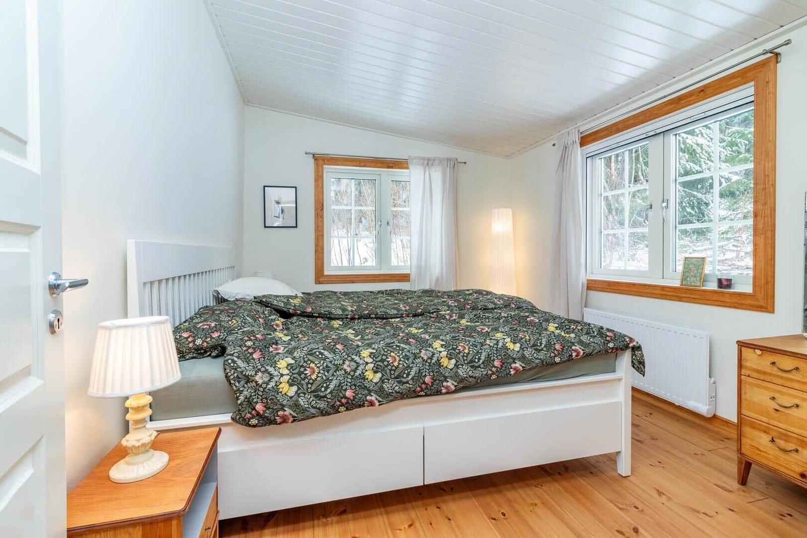 Schlafzimmer mit Bett, Fenstern und Holzboden.