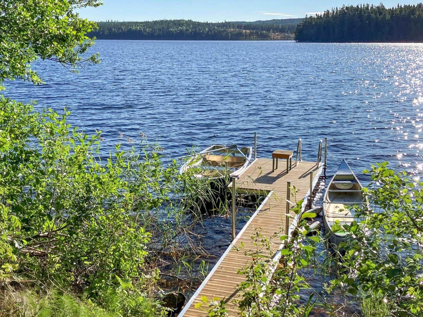 Holzsteg mit zwei Booten am Ufer eines Sees mit Wald im Hintergrund.