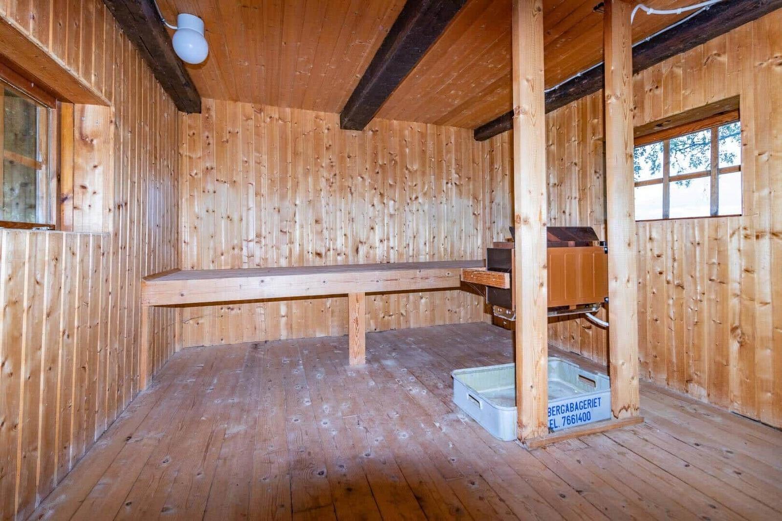 Holzsauna mit Bank, Ofen und Fenstern. Boden und Wände aus Holz.