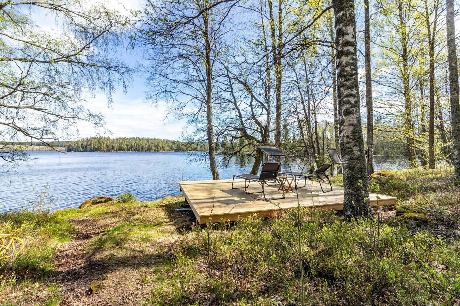 Holzterrasse mit Liegestühlen am See, umgeben von Bäumen.