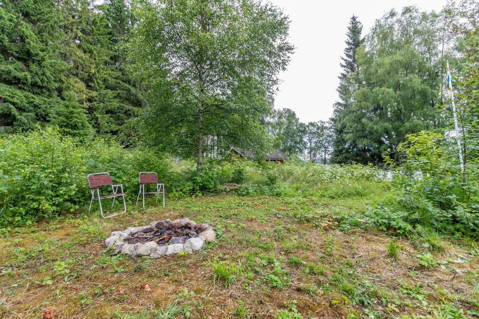 Feuerstelle mit Steinen und zwei Stühlen im Wald. Hintergrund: Holzhütte.