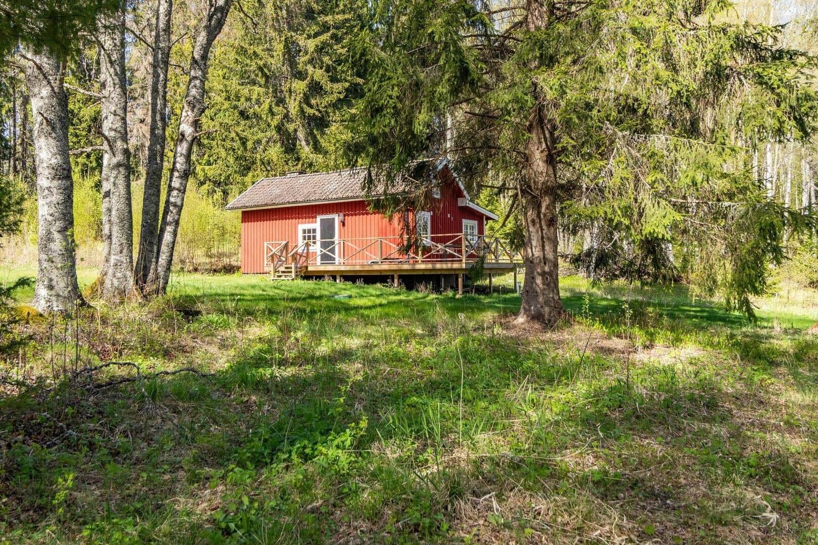 Rotes Holzhaus mit Veranda im Wald. Grasland und Bäume umgeben die Unterkunft.