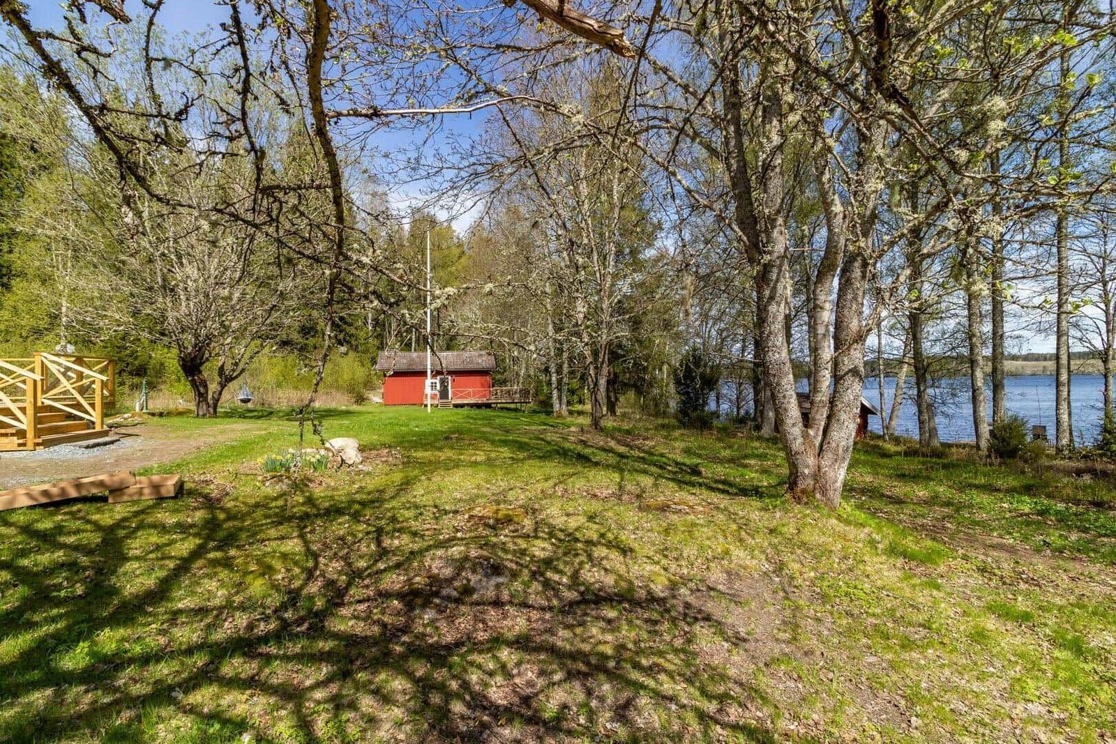 Rotes Haus mit Terrasse im Wald, Blick auf See und grünes Gras.