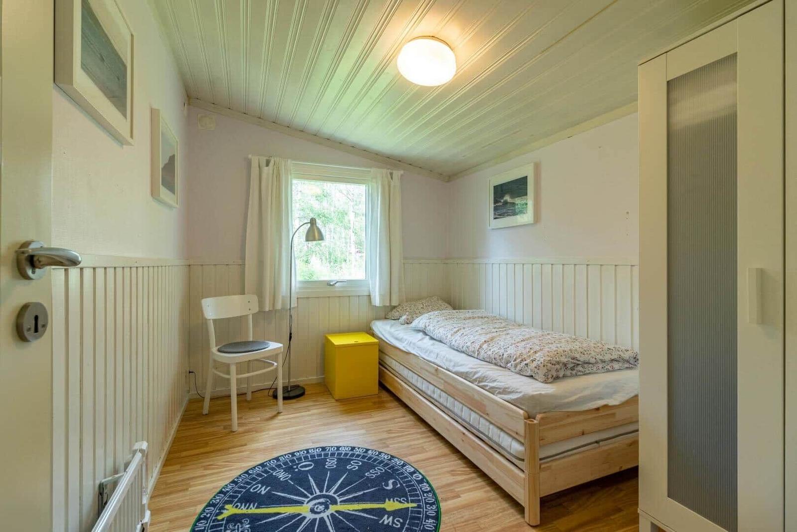 A bedroom with a bed, a chair, a window, and a round rug.