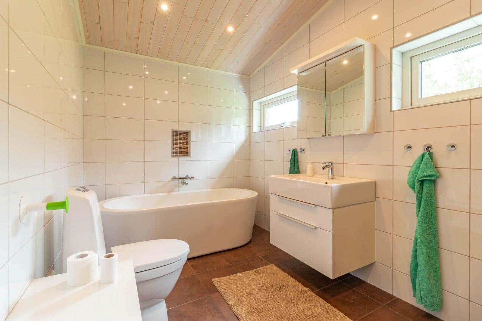 Bathroom with bathtub, sink and toilet. Wooden ceiling and green towels.