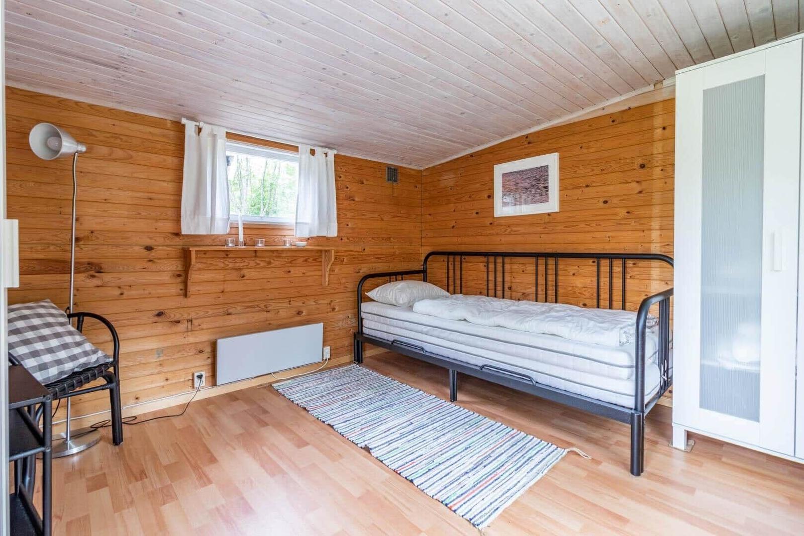 Bedroom with wooden walls, bed, wardrobe, and window with curtains.