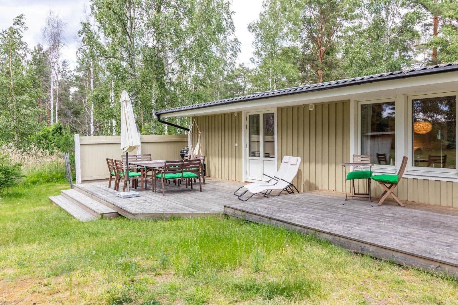Deck with table, chairs, lounge chair, and grill. Background: forest.