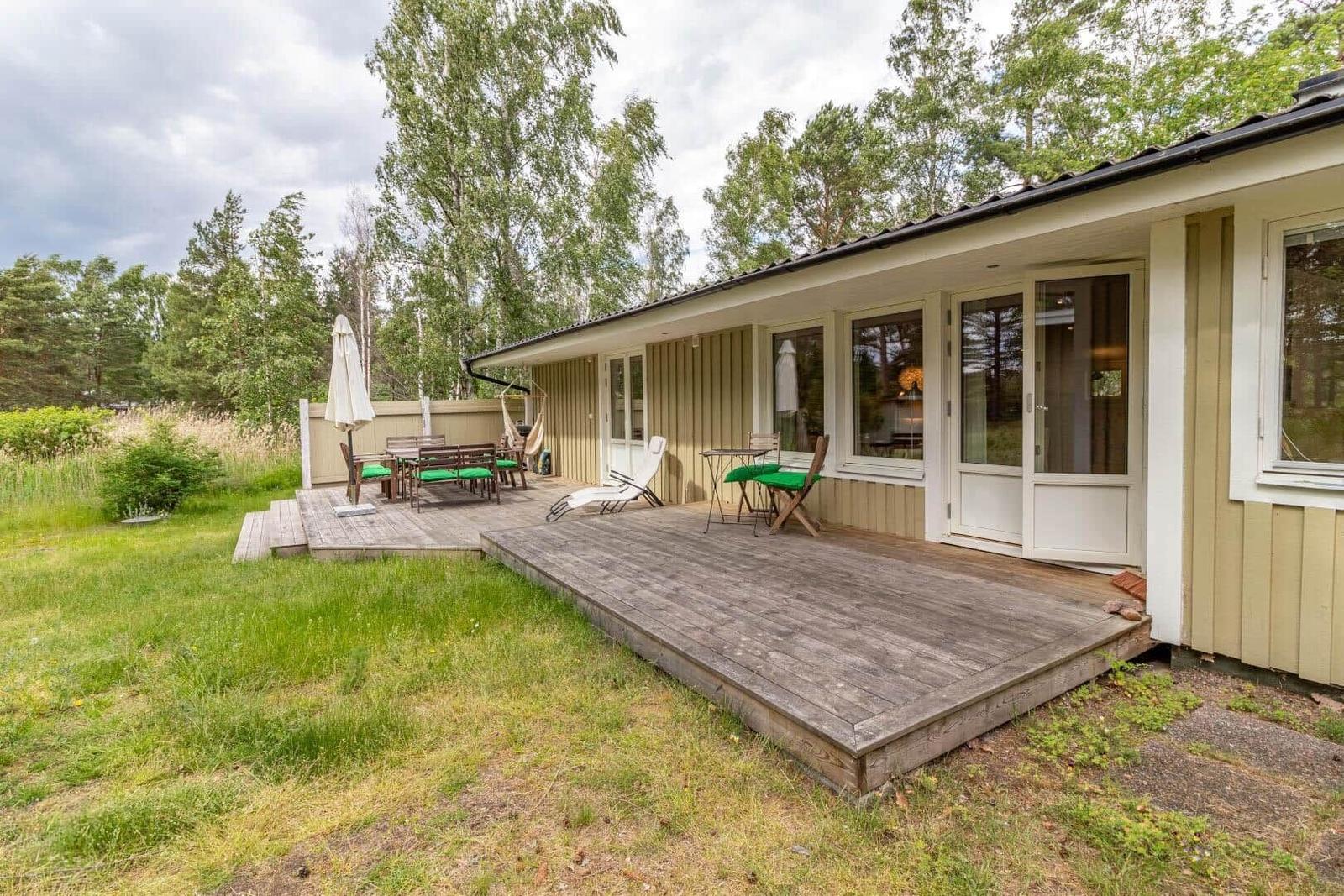 House with terrace, garden, and outdoor seating. Wooden terrace with tables and chairs.