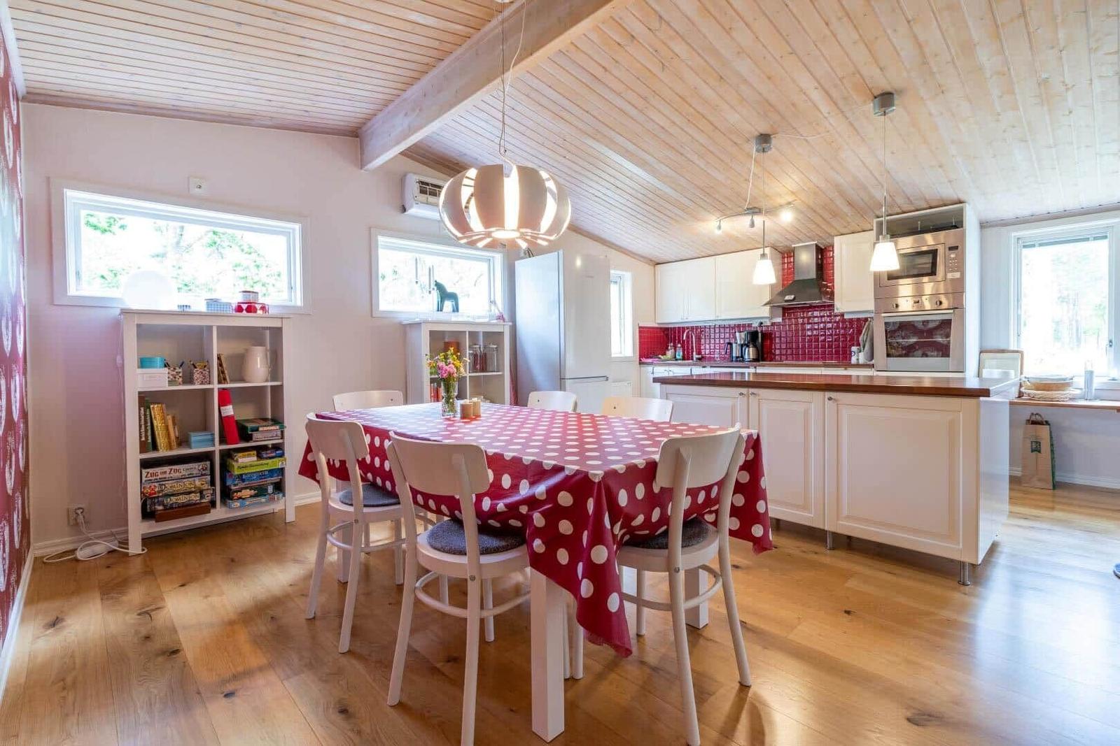 Dining area with table, chairs, and red tablecloth. Kitchen with countertop and appliances.