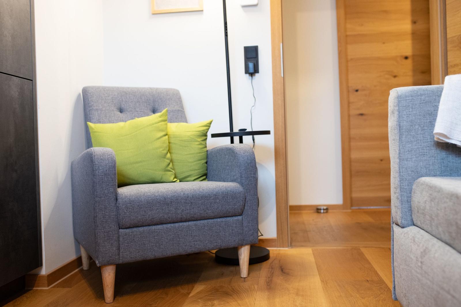 Ein grauer Sessel mit zwei grünen Kissen steht auf Holzfußboden.
