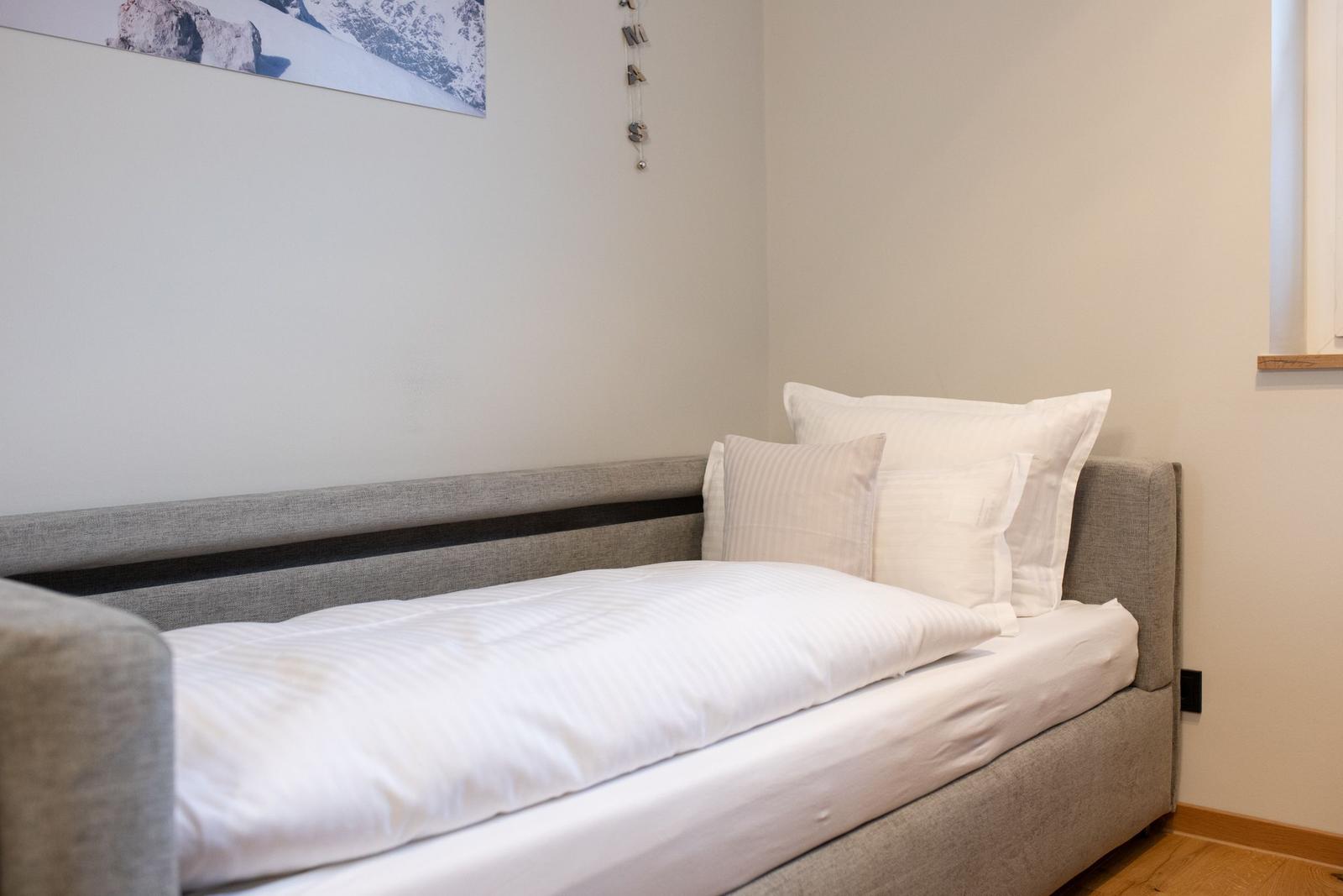 Ein Bett mit weißen Kissen und Bettwäsche. An der Wand hängt ein Bergbild.