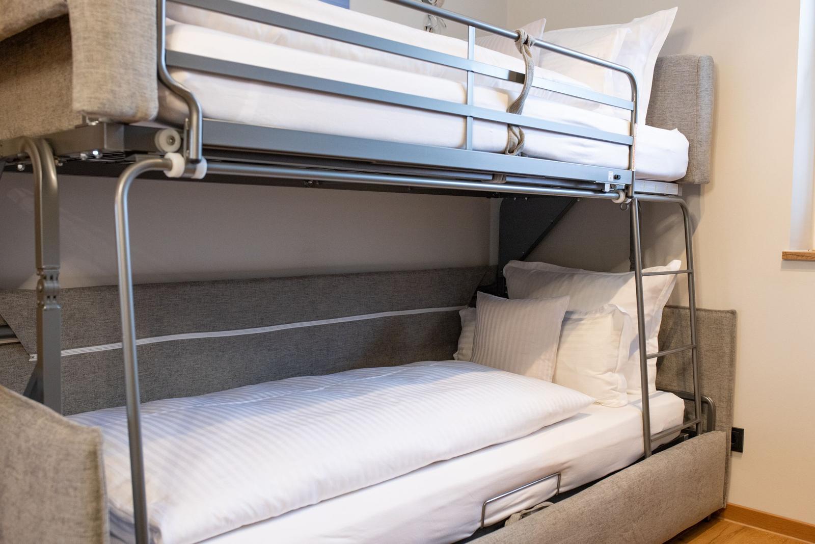 Doppelstockbett mit Matratzen und Kissen. Metallgestell und graue Polsterung.