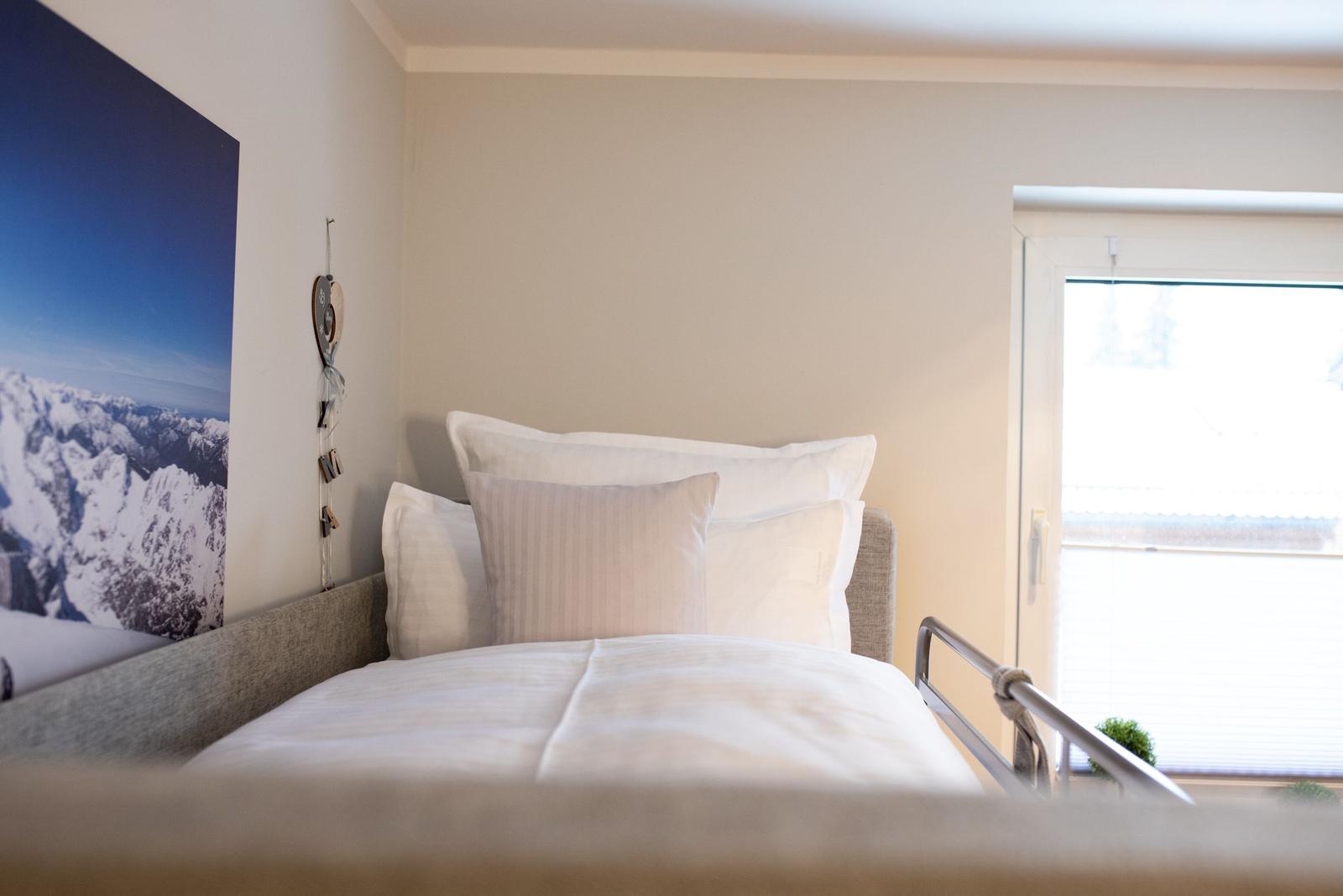 Ein Bett mit weißen Kissen und einer Bettdecke. An der Wand hängt ein großes Wandbild.