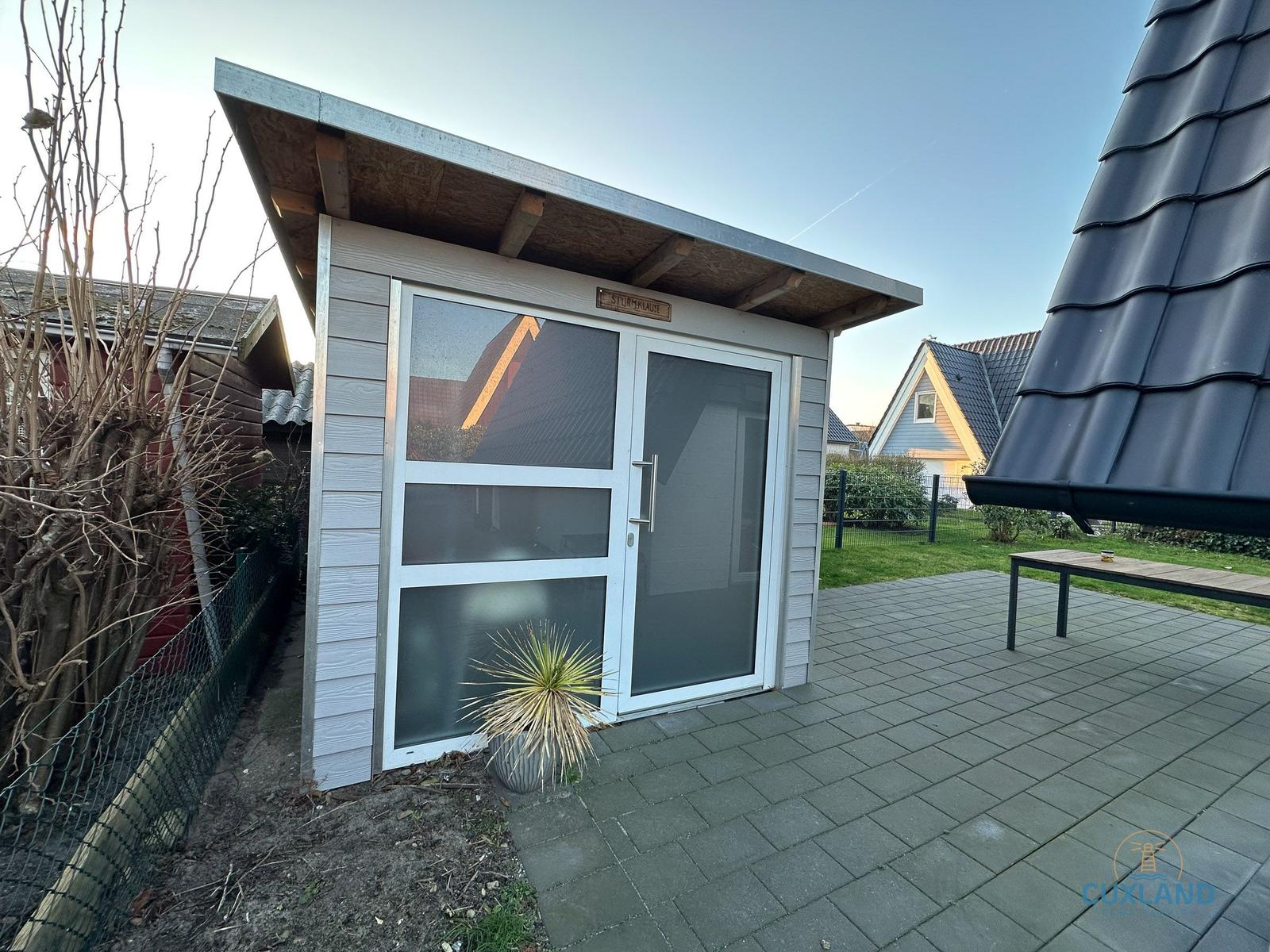 Eine Sturmhaube mit Glasfront und Holzverkleidung auf einer Terrasse.