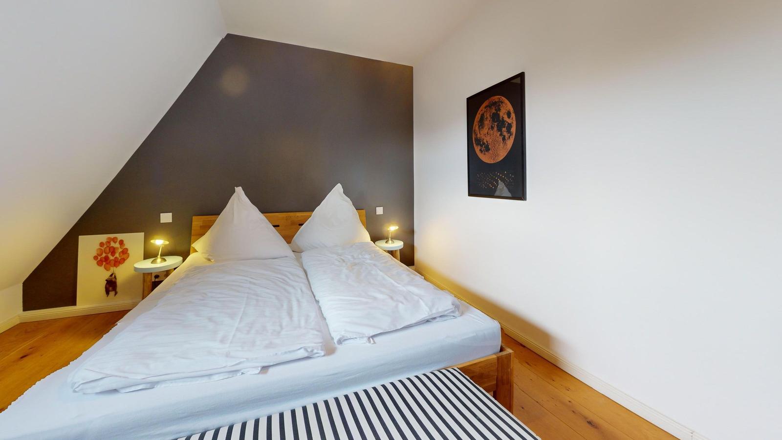 Schlafzimmer mit Doppelbett, Holzboden und Wandbild mit Mond.