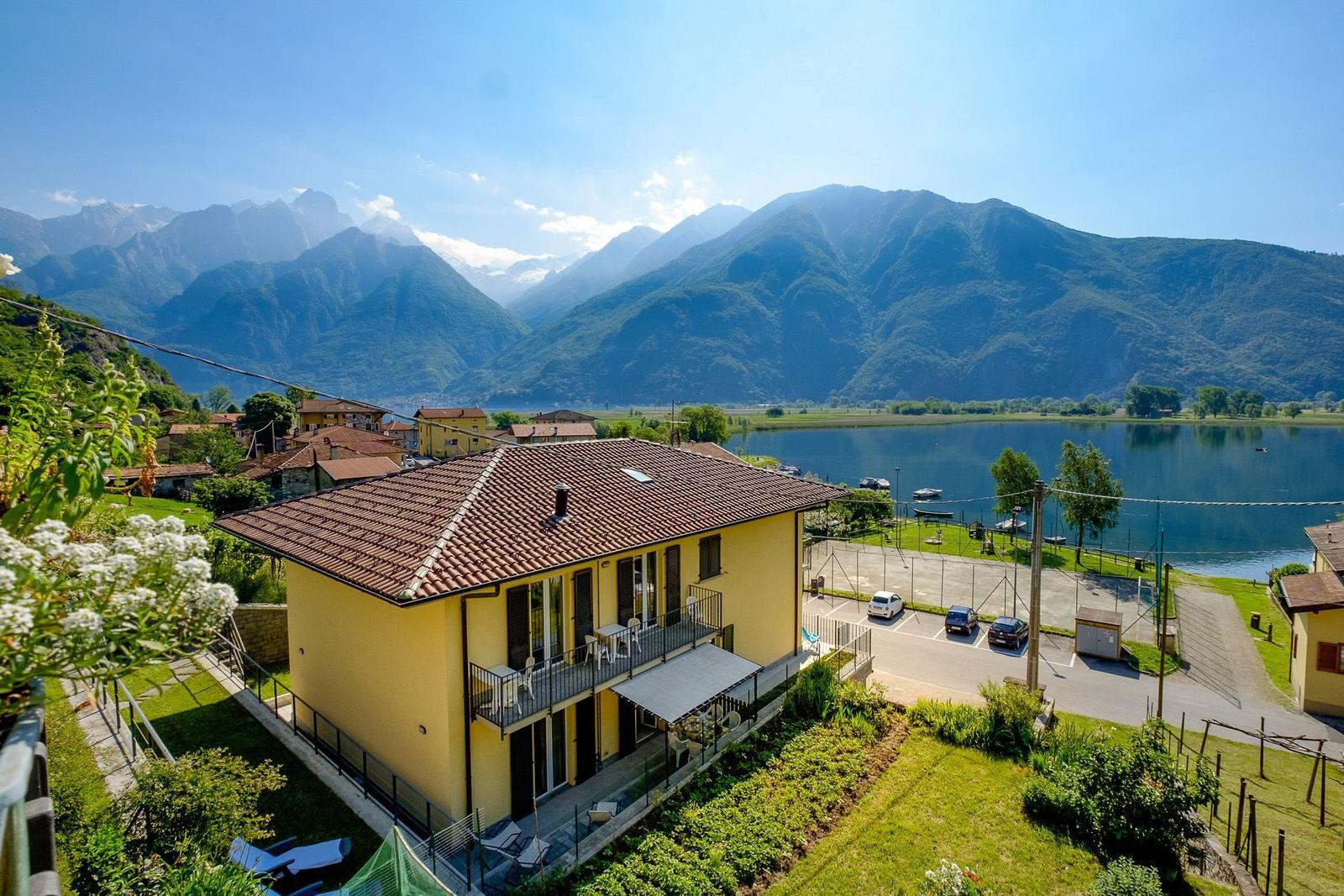 Gelbes Haus mit Balkon, Garten und Blick auf See und Berge.