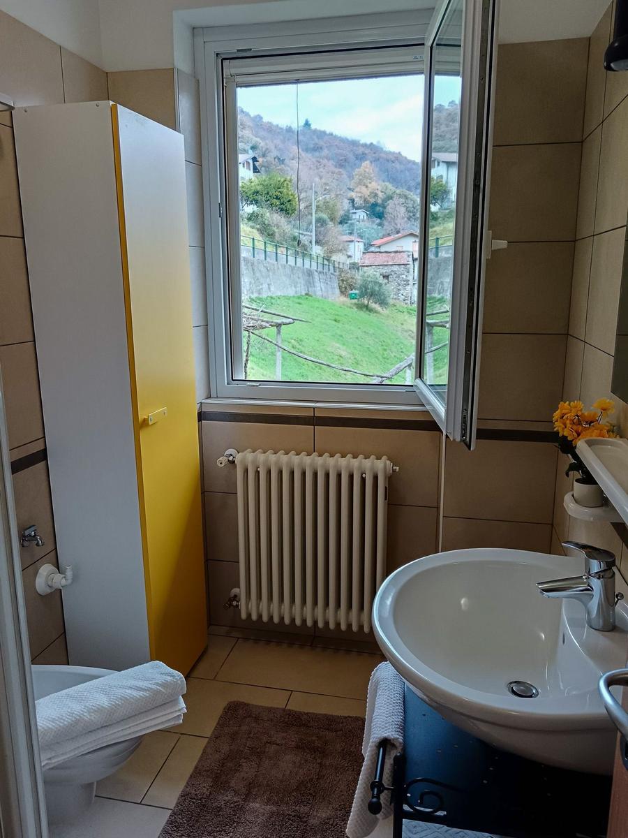 Badezimmer mit Waschbecken, Toilette und Fensterblick auf grüne Hügel.