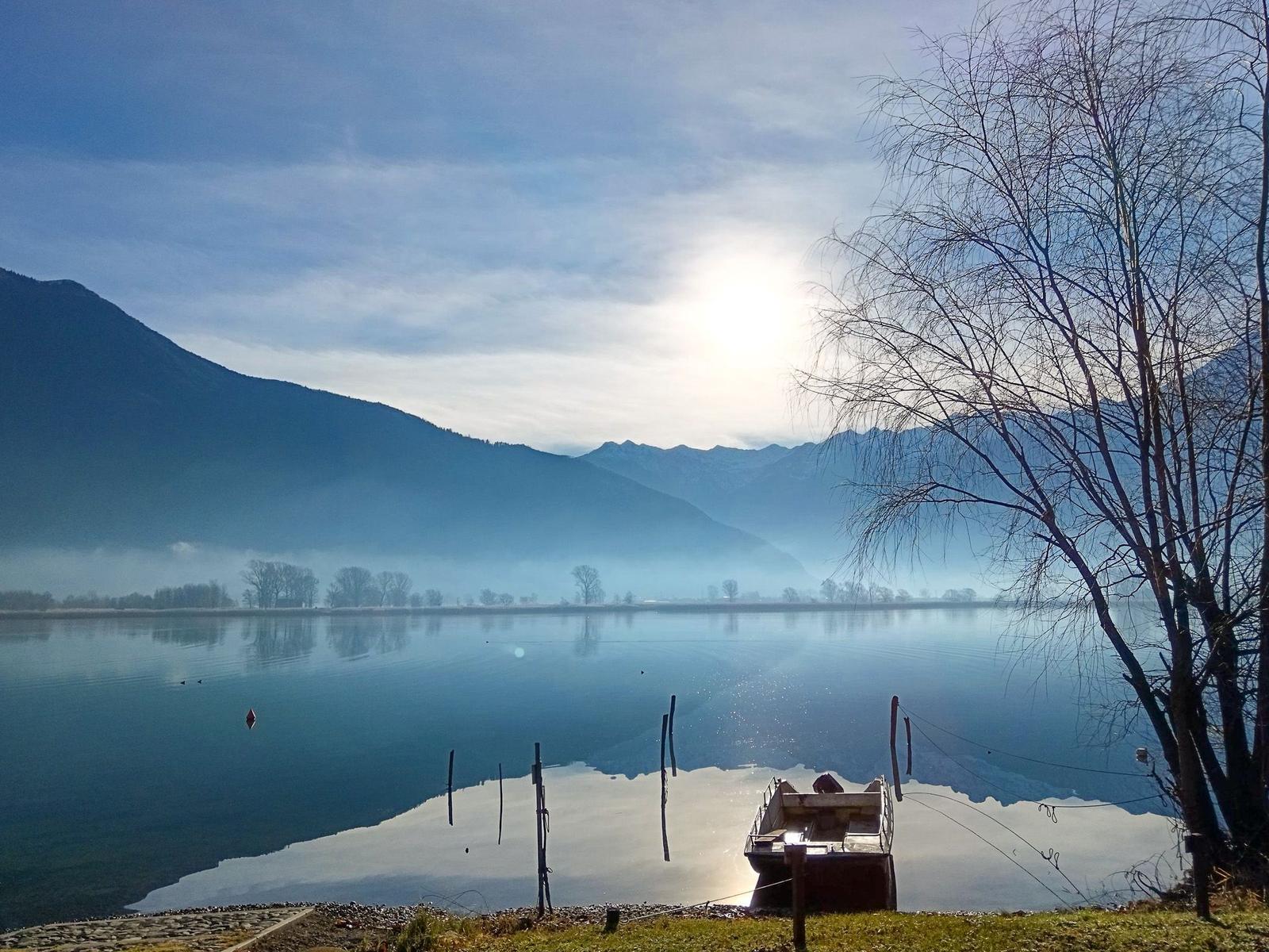 Ein kleines Boot liegt am Ufer eines Sees, umgeben von Bergen und Bäumen.
