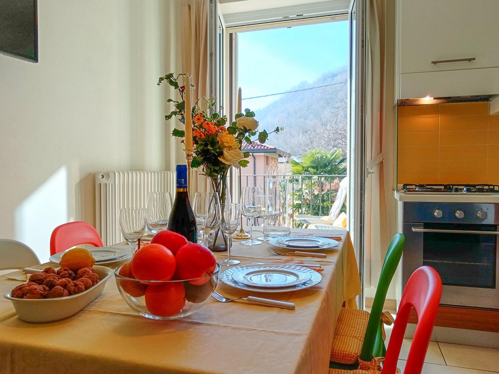 Esstisch mit Obst, Wein und Blick auf Balkon und Berge.