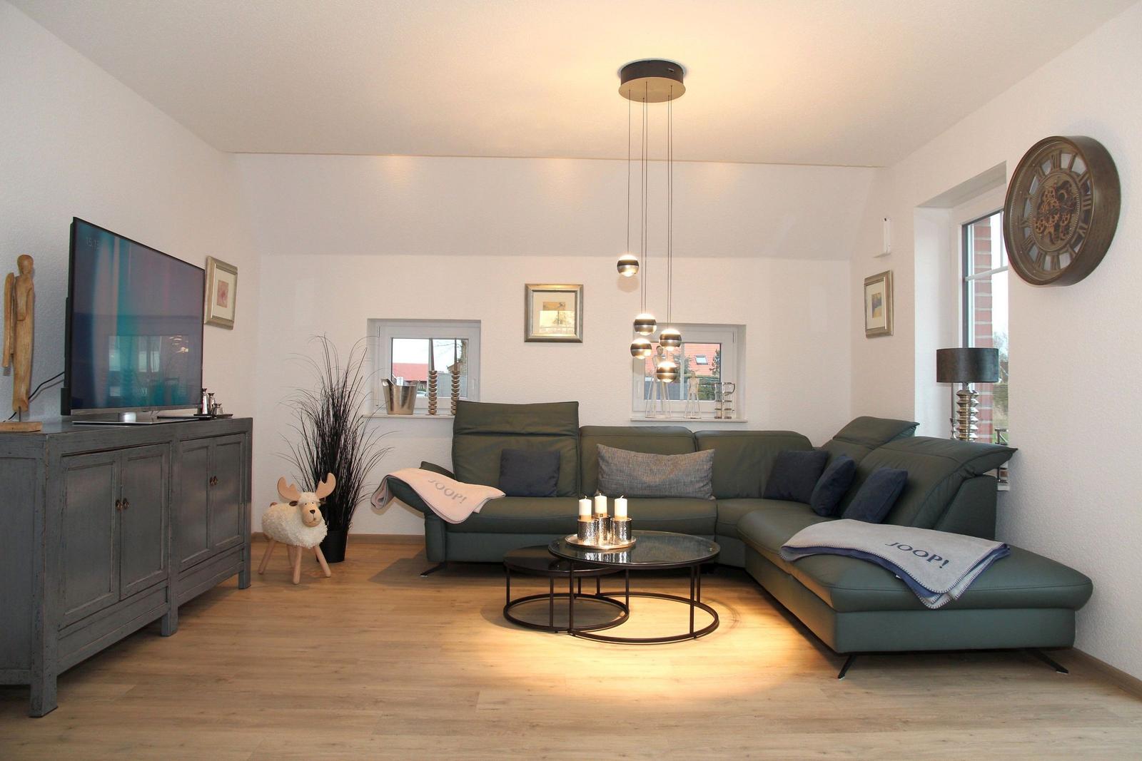 Wohnzimmer mit grünem Sofa, Glas-Tisch und Fernseher auf grauem Schrank.